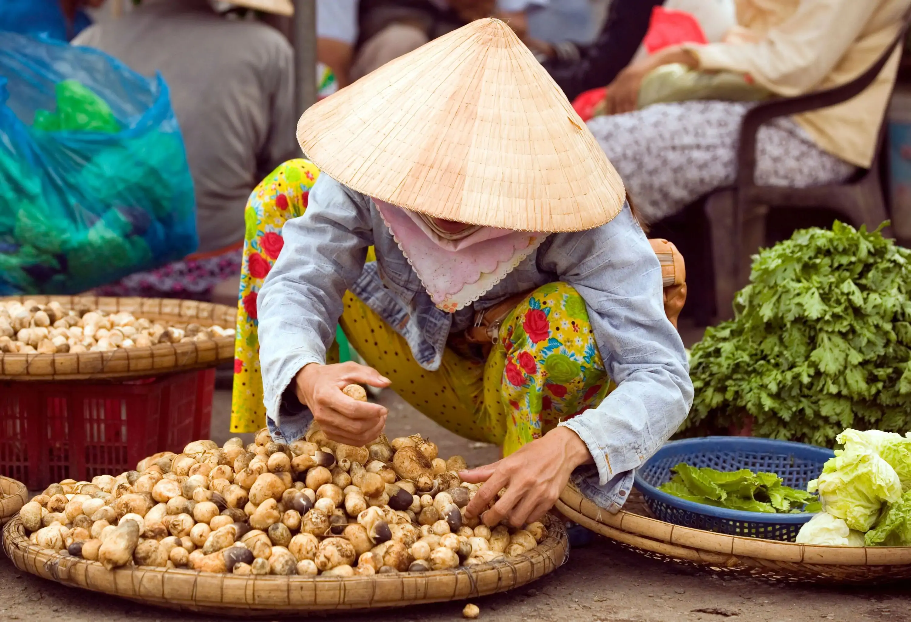 A market vendor wearing a traditional leaf hat carefully arranged his products on a basket in the street.