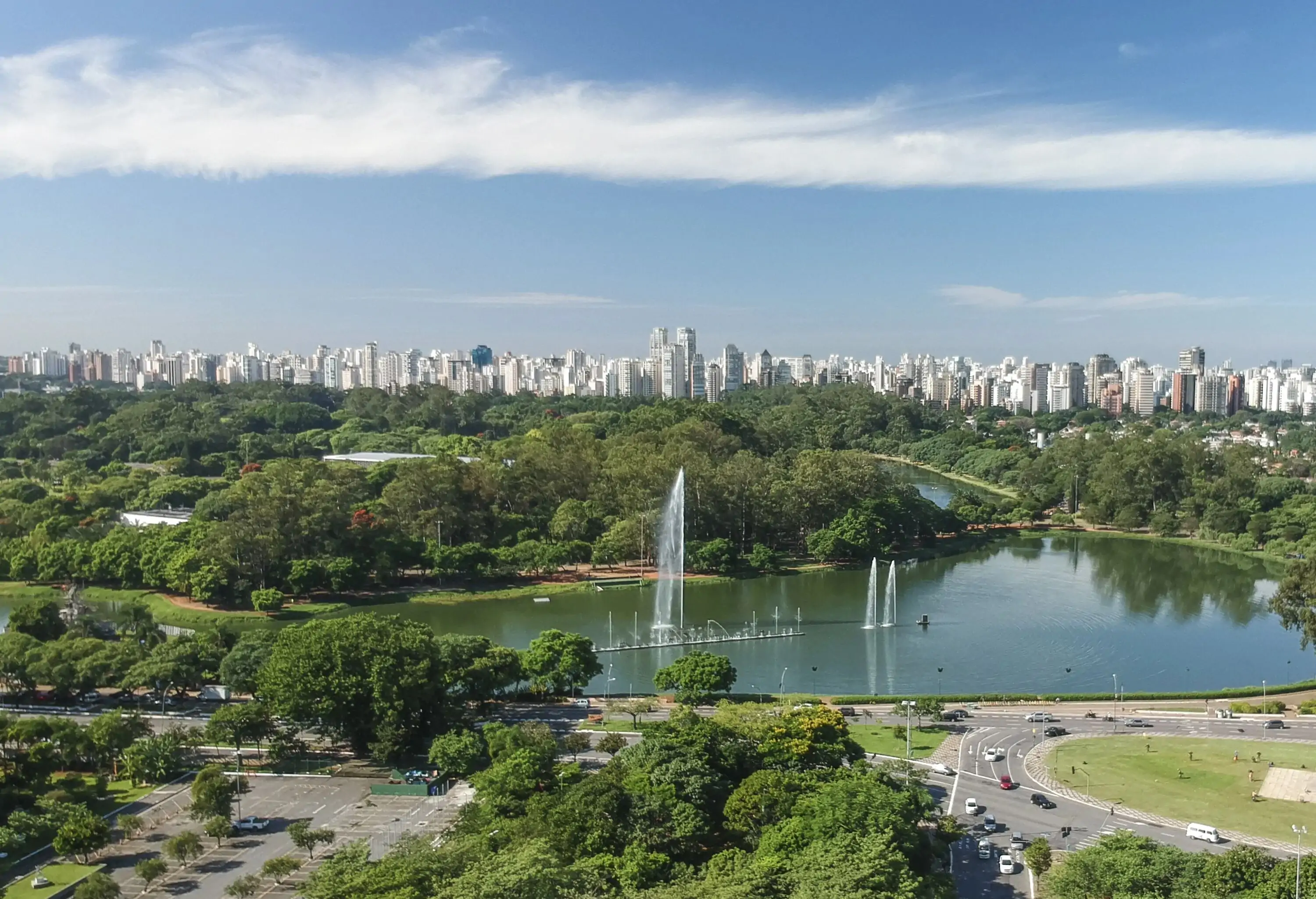 A water fountain on a pond is one of the attractions in the lush green park against the city skyline.