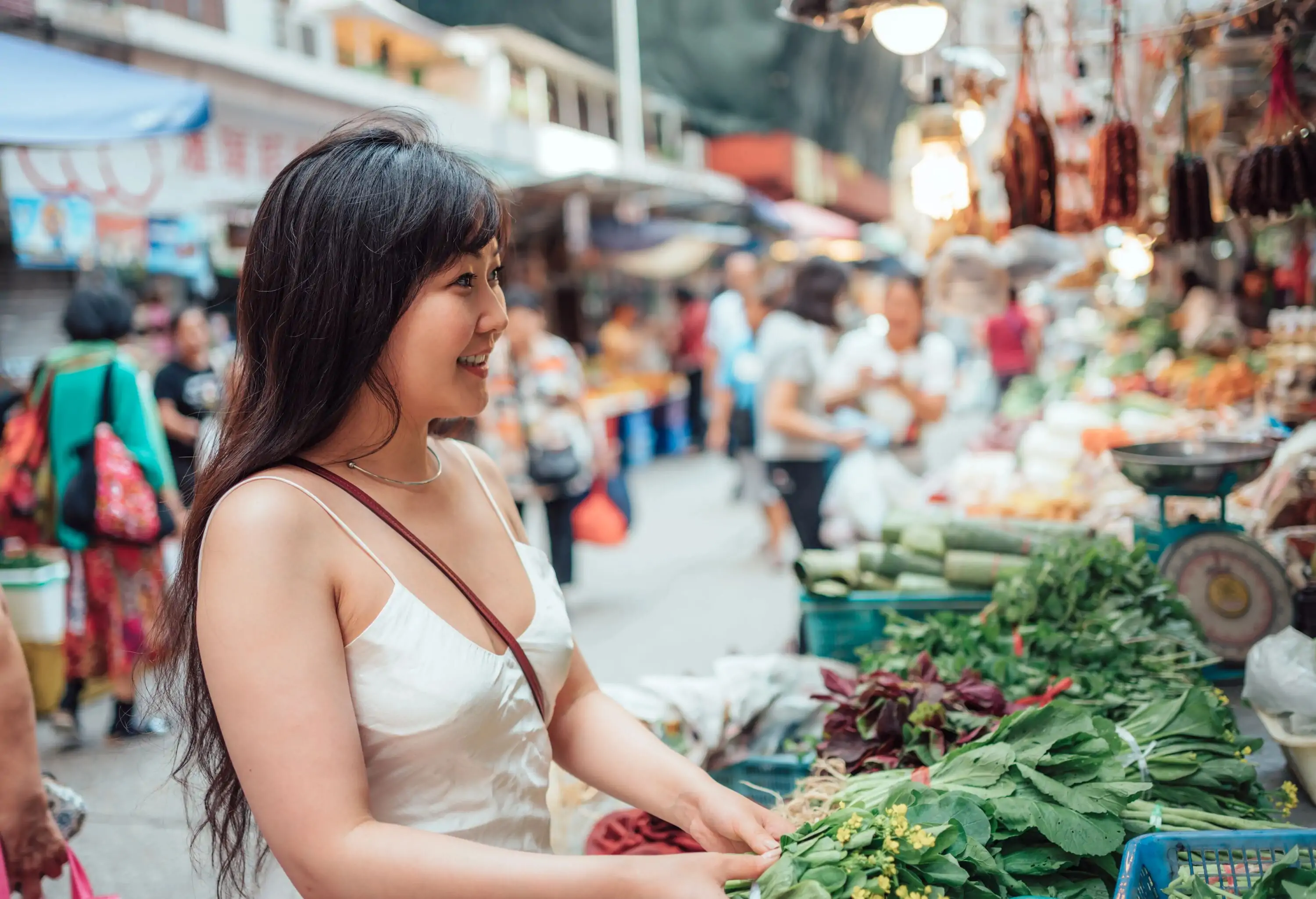 A long-haired woman buying vegetables in a market vendor stall.