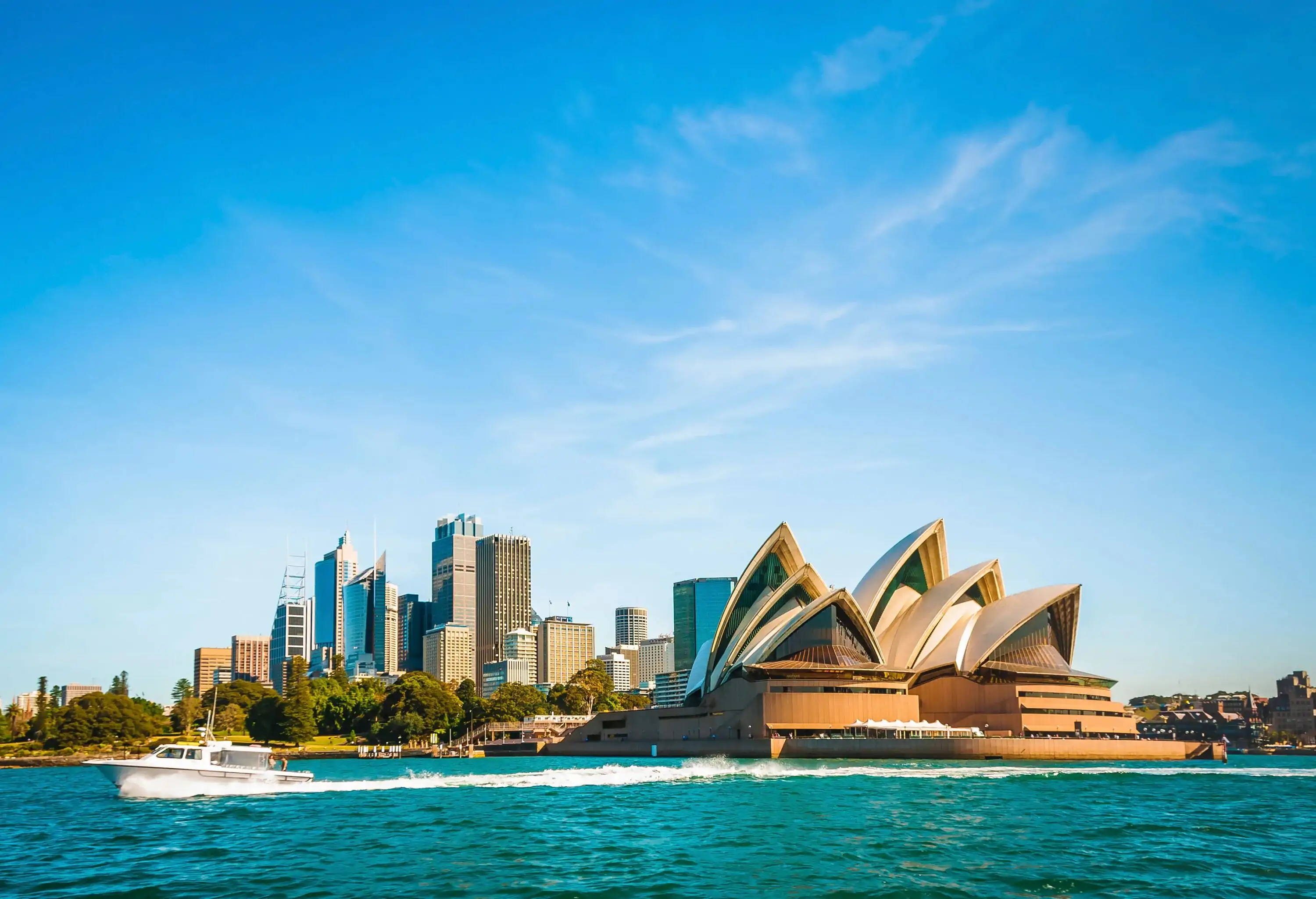 A boat speeding by the Sydney Opera House during the day.