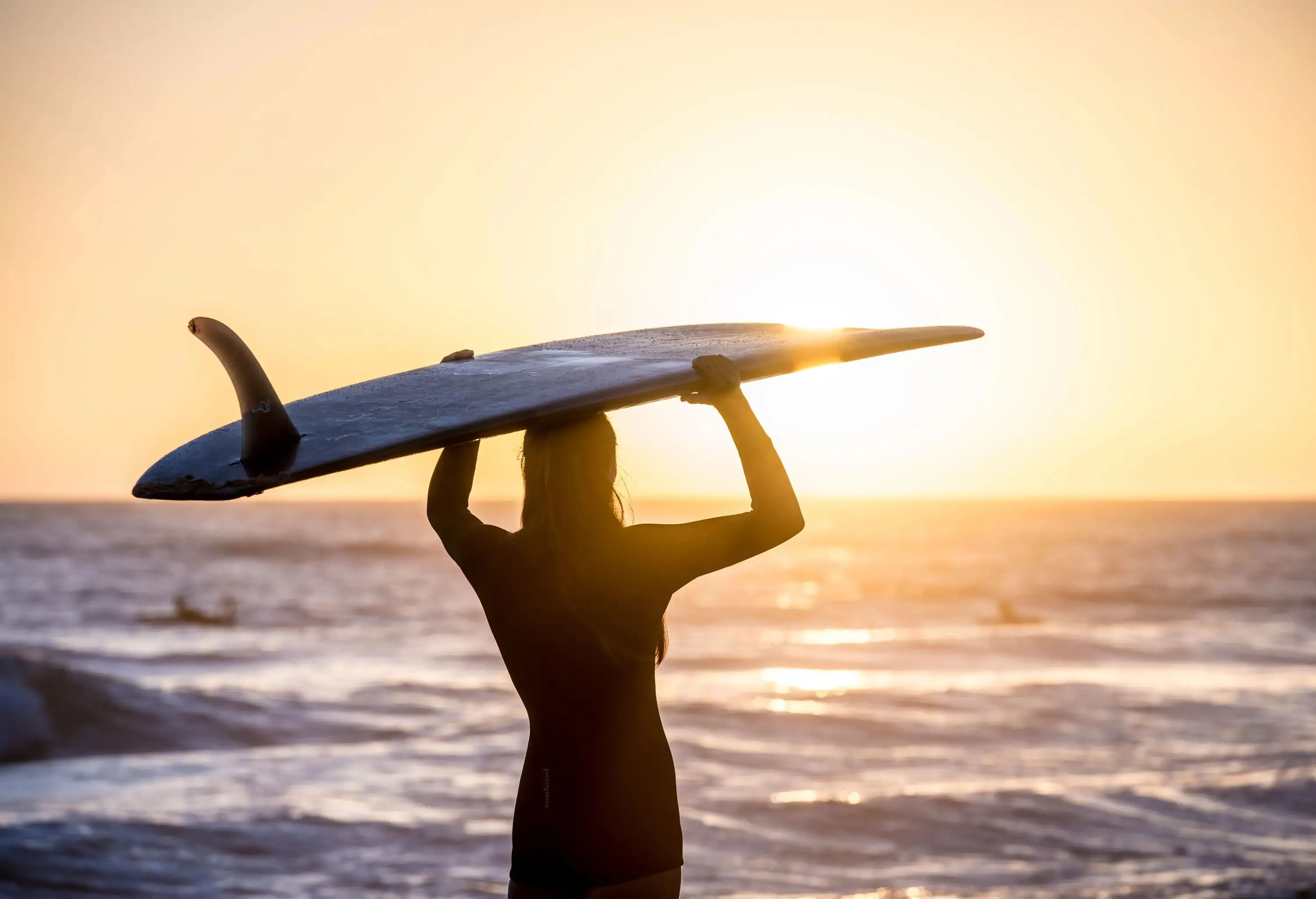 A shadow of a woman with a surfboard over her head standing on the beach.