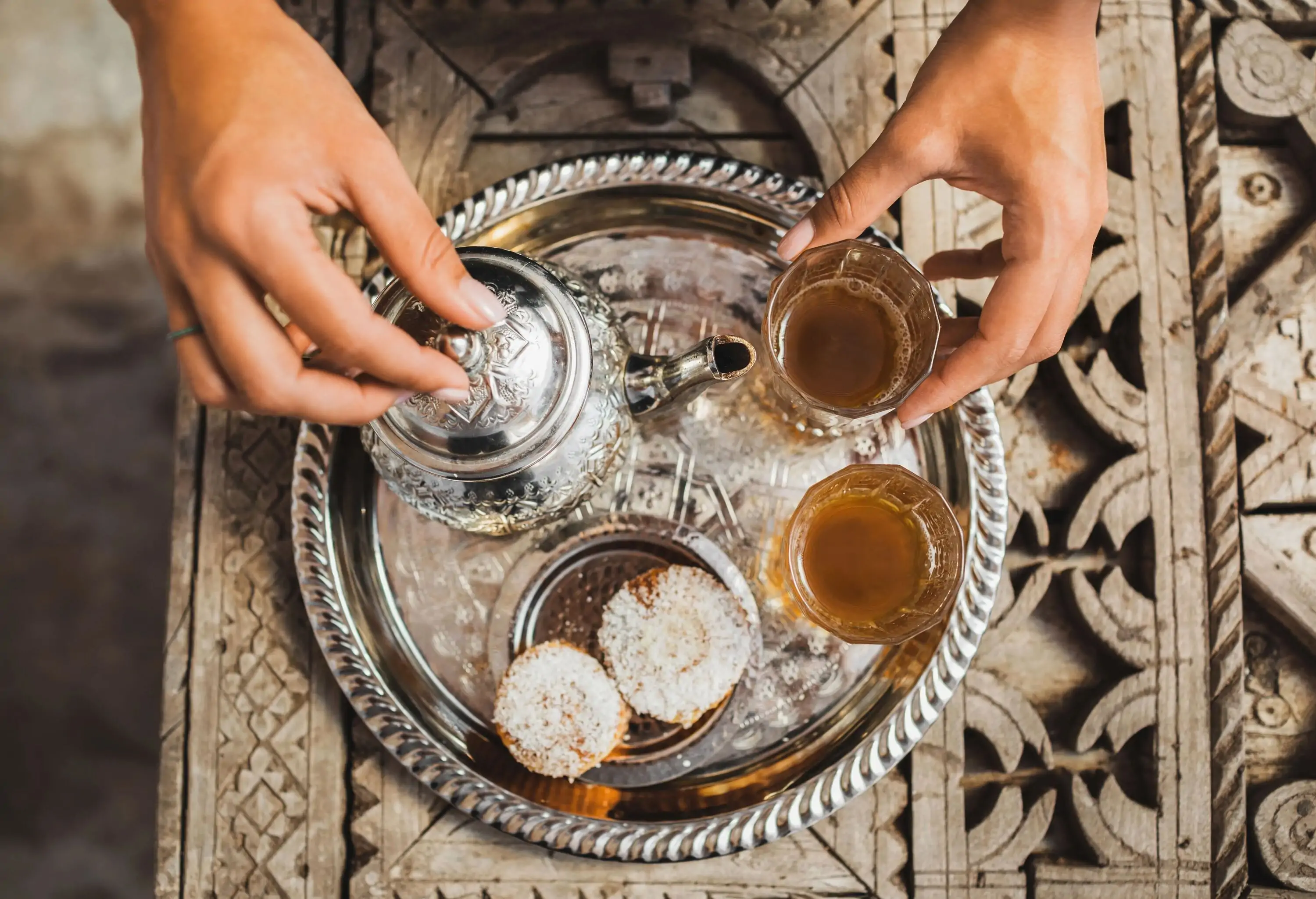 Woman hands serving traditional moroccan mint tea ceremony with cookies and vintage silver teapot. Hospitality and service in Morocco, Marrakech.