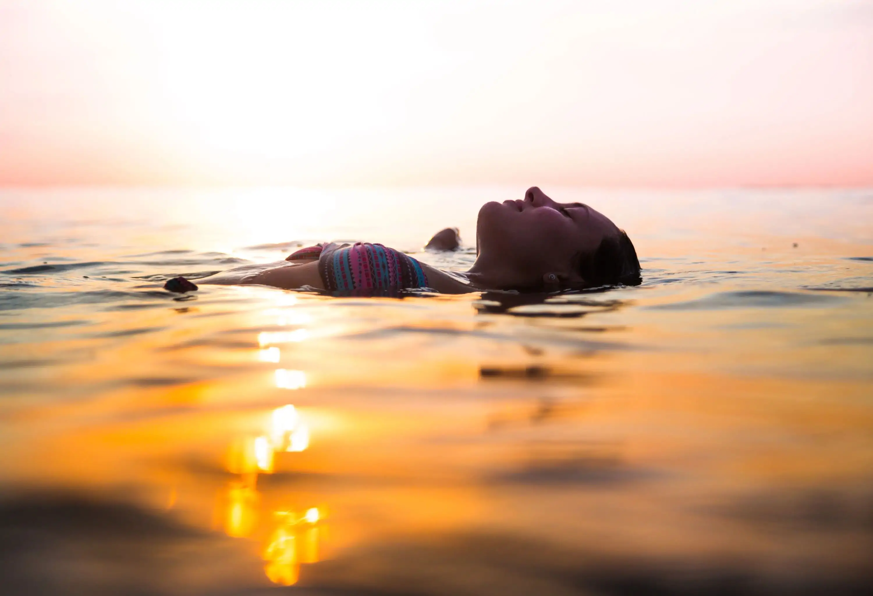 A lady traveller floats on the tranquil water surface of the sea on a dramatic sunset.