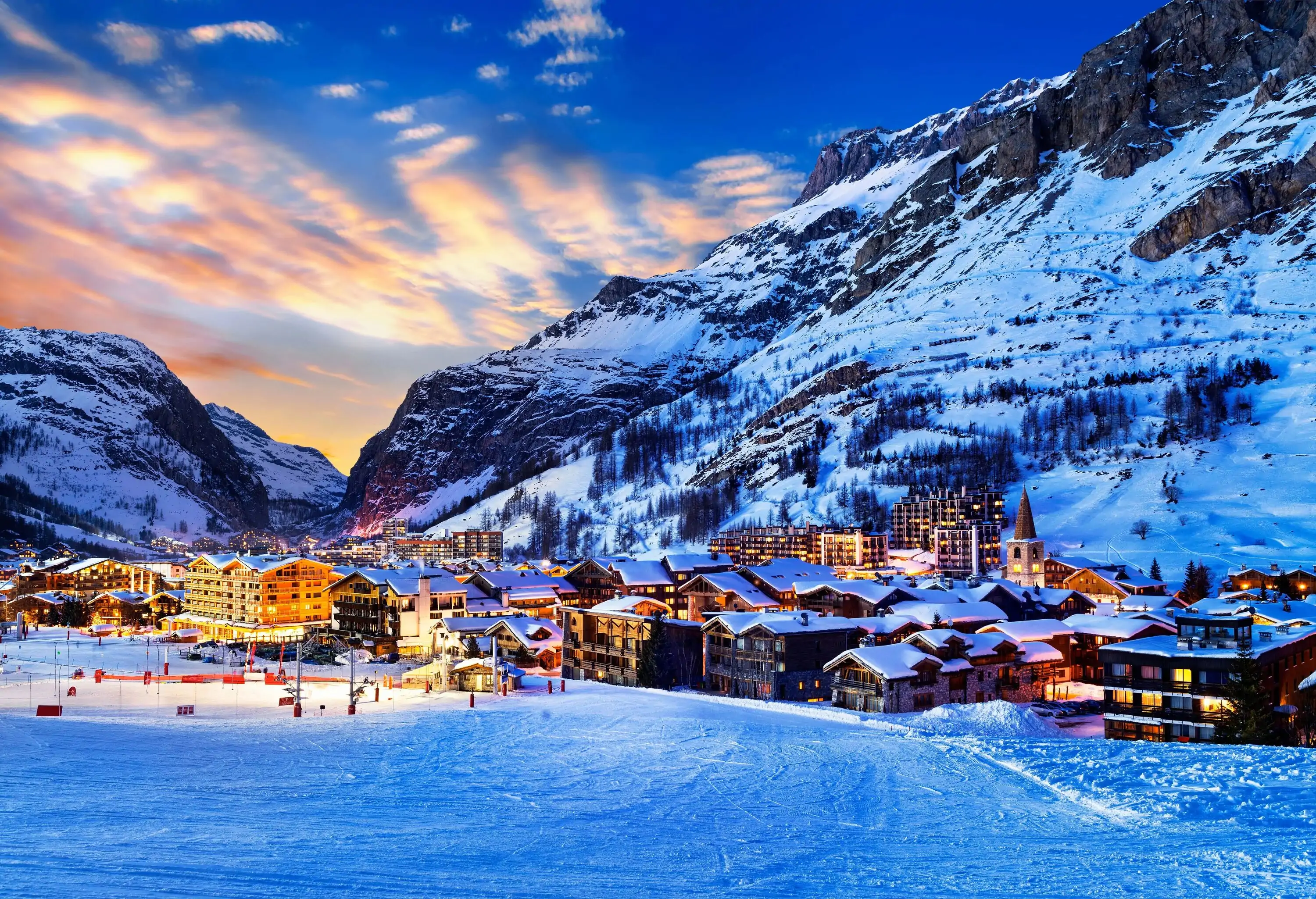 An illuminated ski village surrounded by steep, rugged mountains.