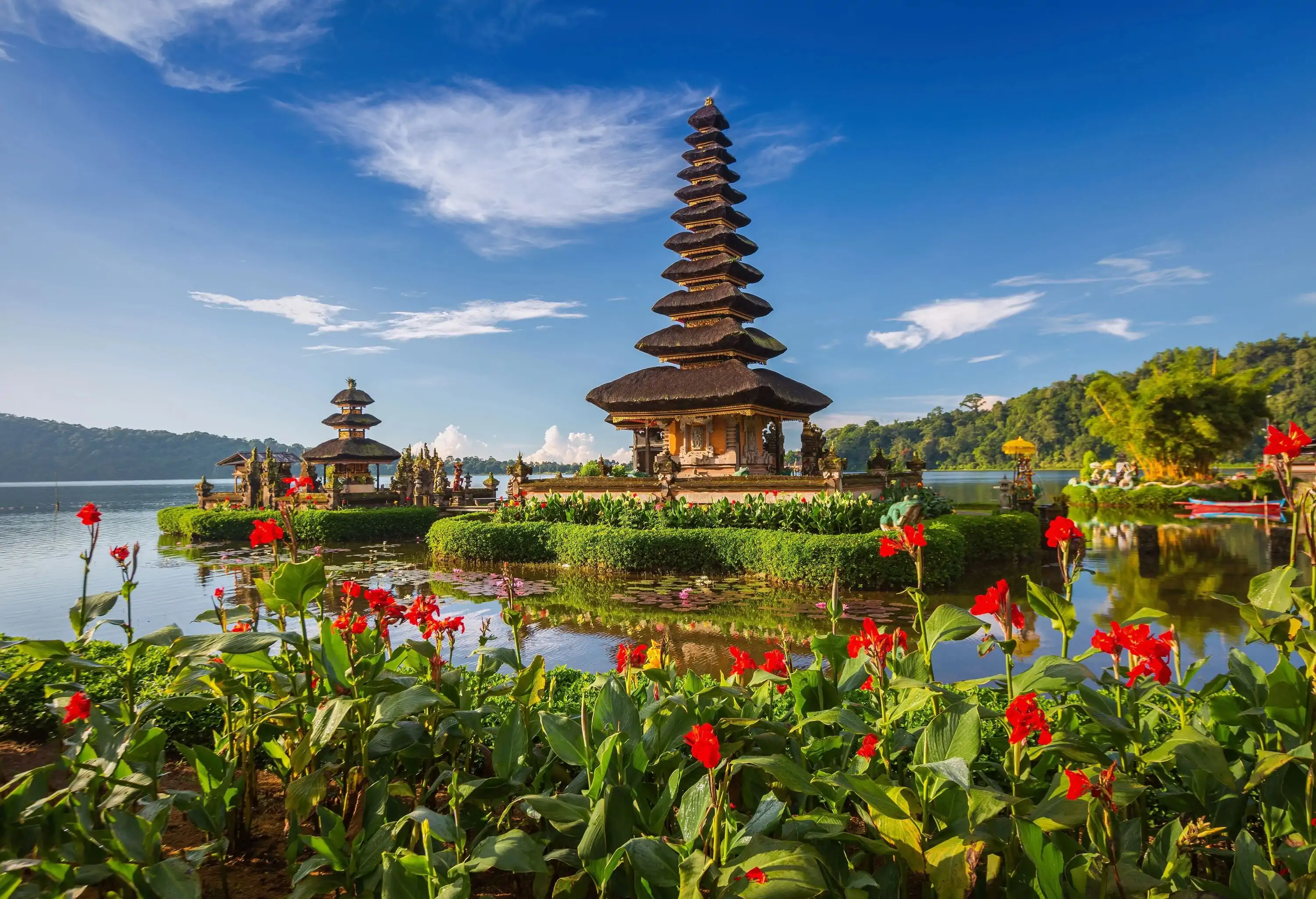 Pura Ulun Danu Bratan is a Hindu temple with multilevel pagoda-style thatched roofs nestled beside a lake and surrounded by a flower garden.