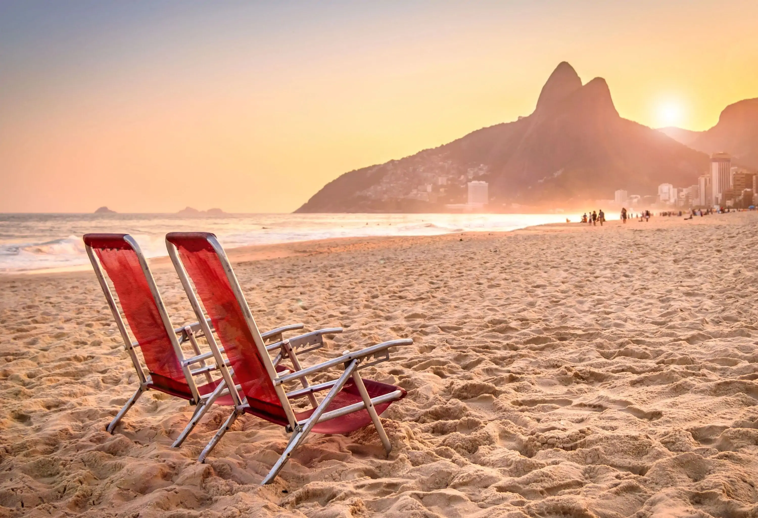 A picturesque beach scene features two deck chairs in the foreground, inviting relaxation and repose, as the iconic Two Brothers Mountain rises majestically in the background.