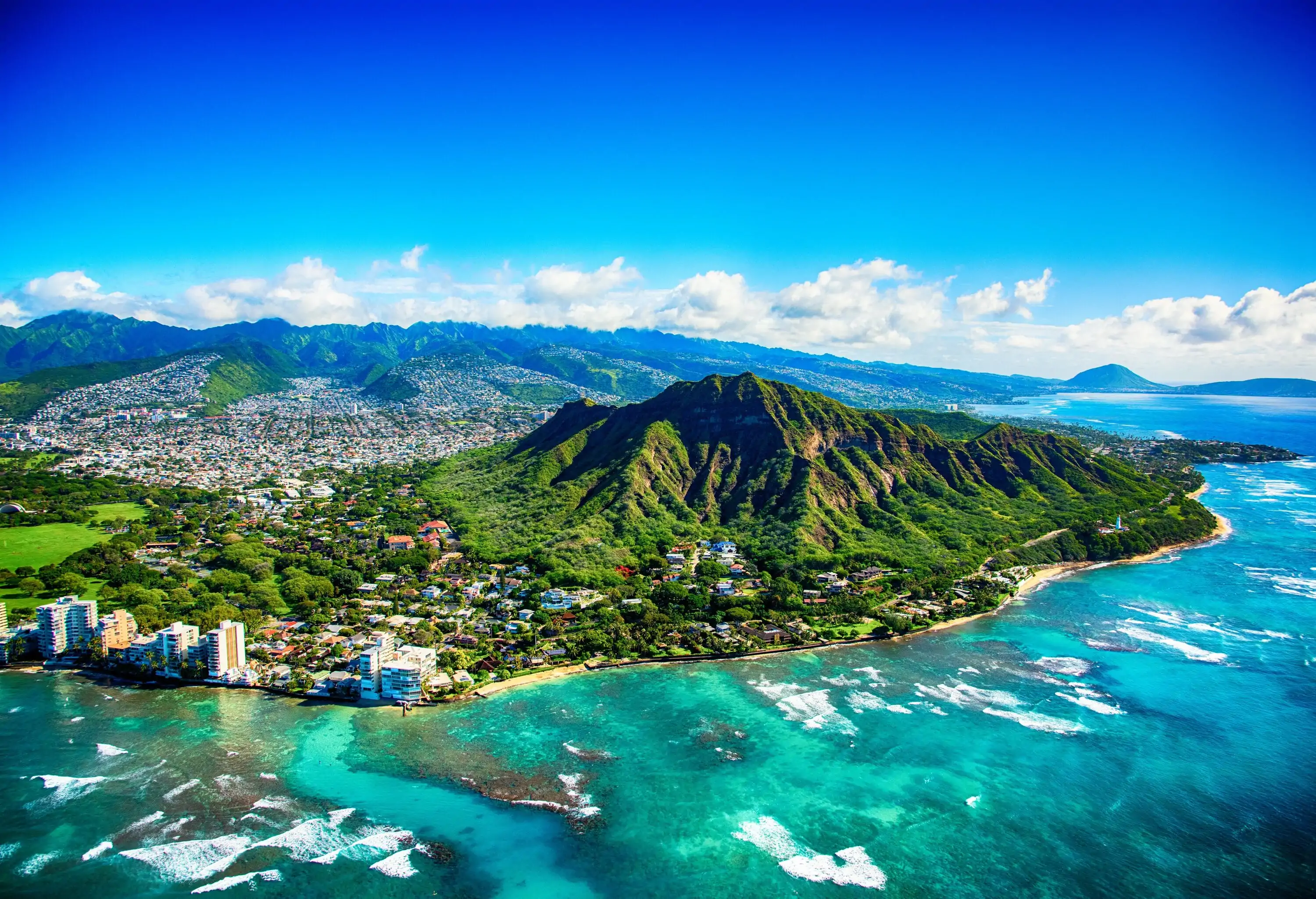 A lush green extinct volcano at the coast's edge surrounded by houses, overlooking a stunning ocean view.