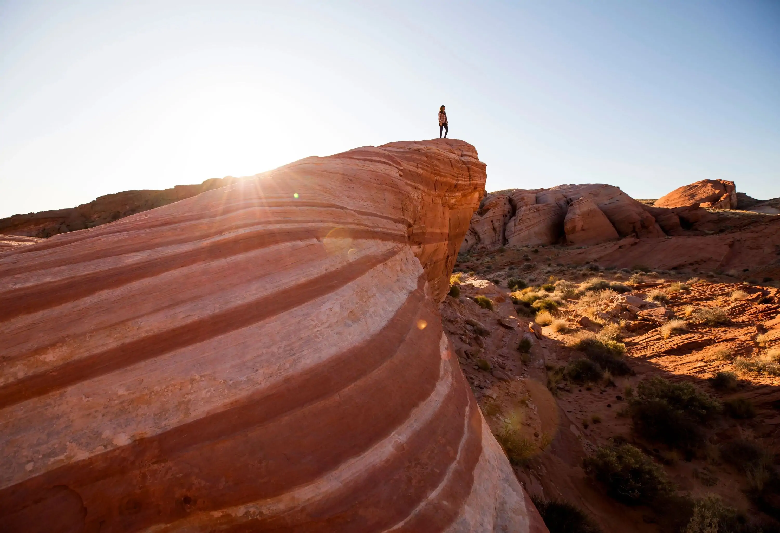 A person stands on the edge of a magnificent rock formation, adorned with captivating streaks and lines, overlooking the vast expanse of a desert landscape.