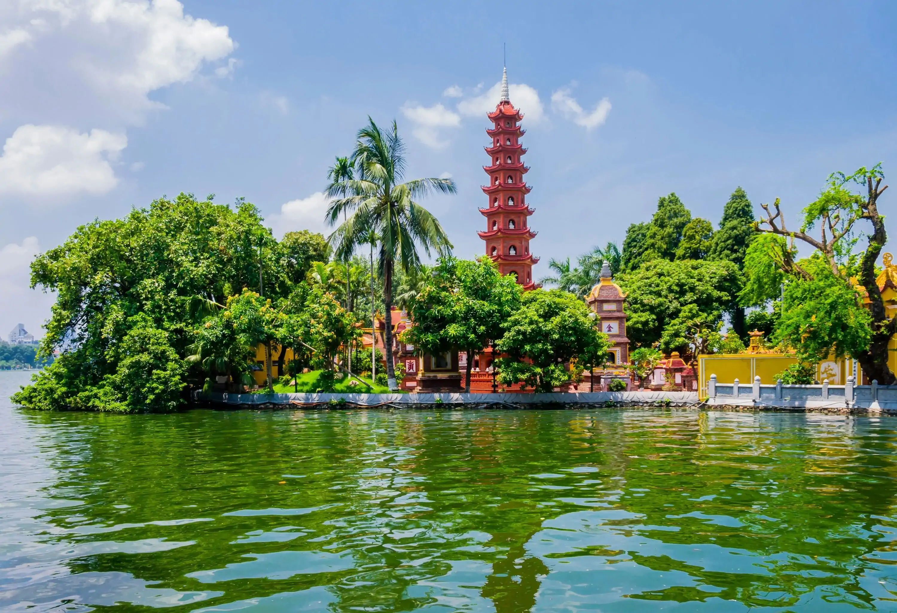 A temple surrounded by trees alongside a green water lake.