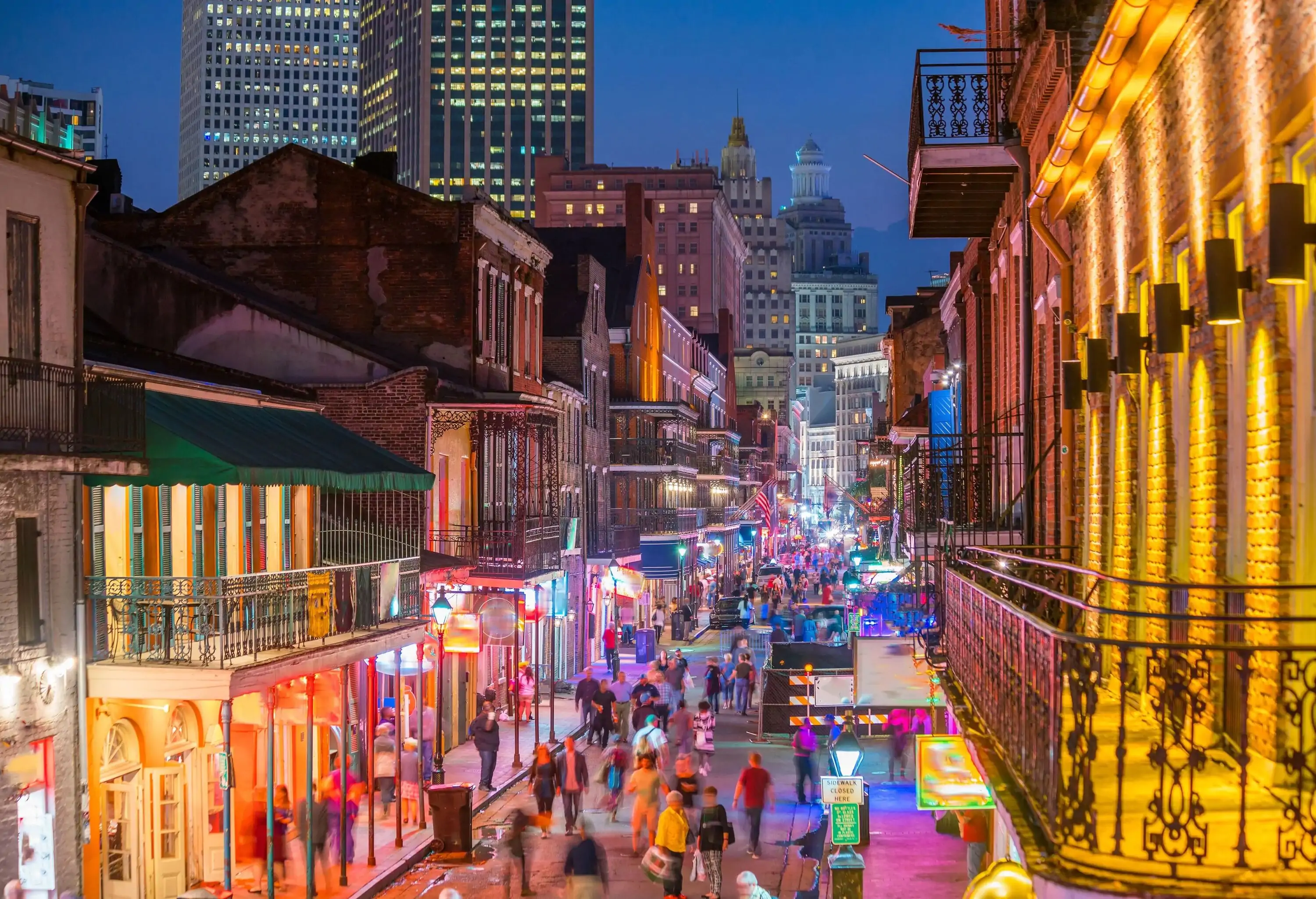 A vibrant avenue coming alive at night with bright lights as people stroll by the stores and restaurants. 