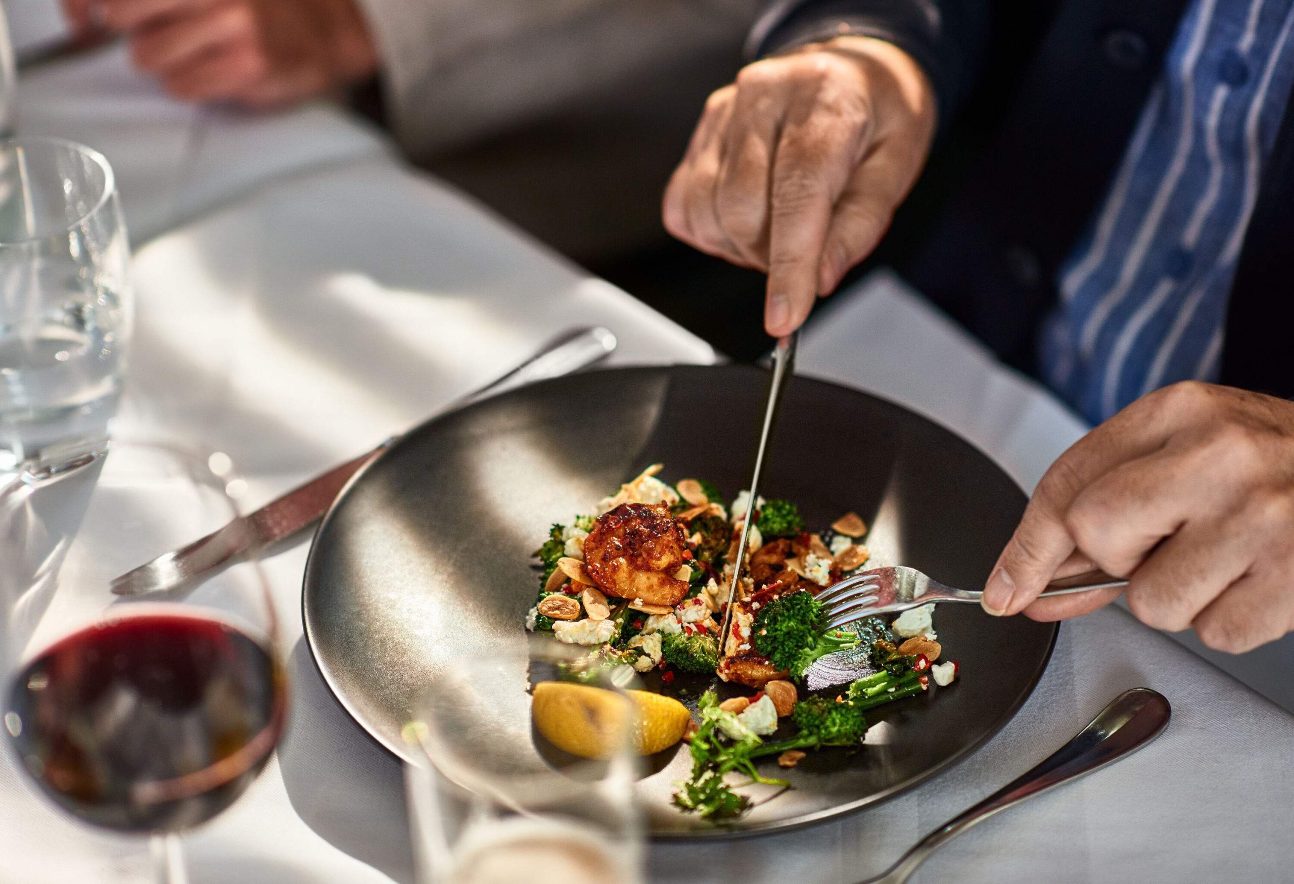 A man eating his food with wine in a restaurant.