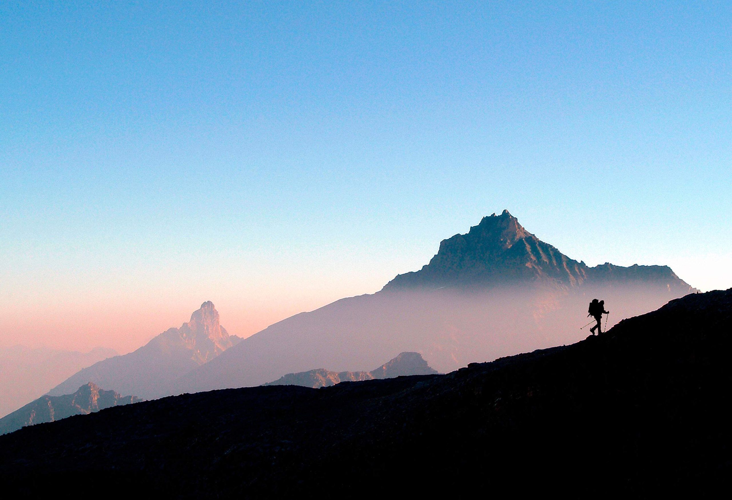 A silhouette of a hiker striding on a ridge with beautiful mountain peaks in the background.