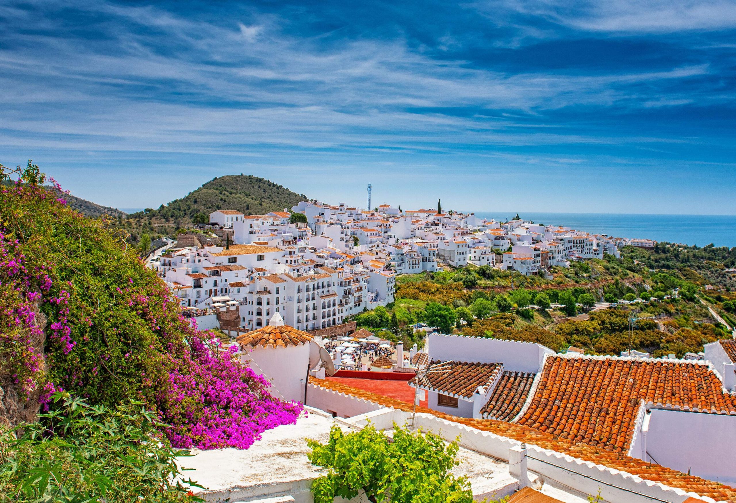 A community of white houses constructed on a hill and surrounded by vegetation provides a view of the vast blue ocean.