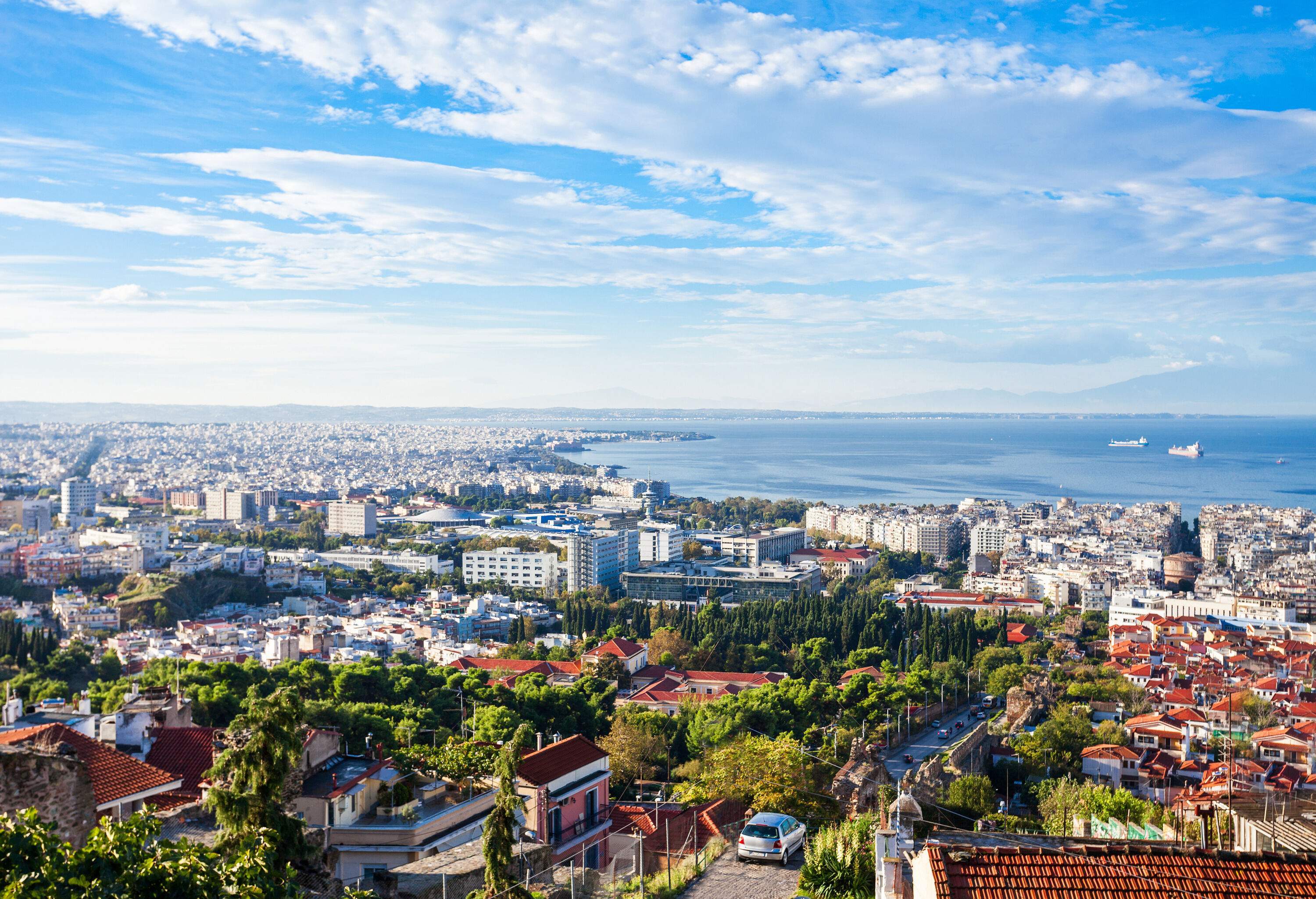 A residential neighbourhood with an overlooking view of a city's urban landscape and a vast ocean.