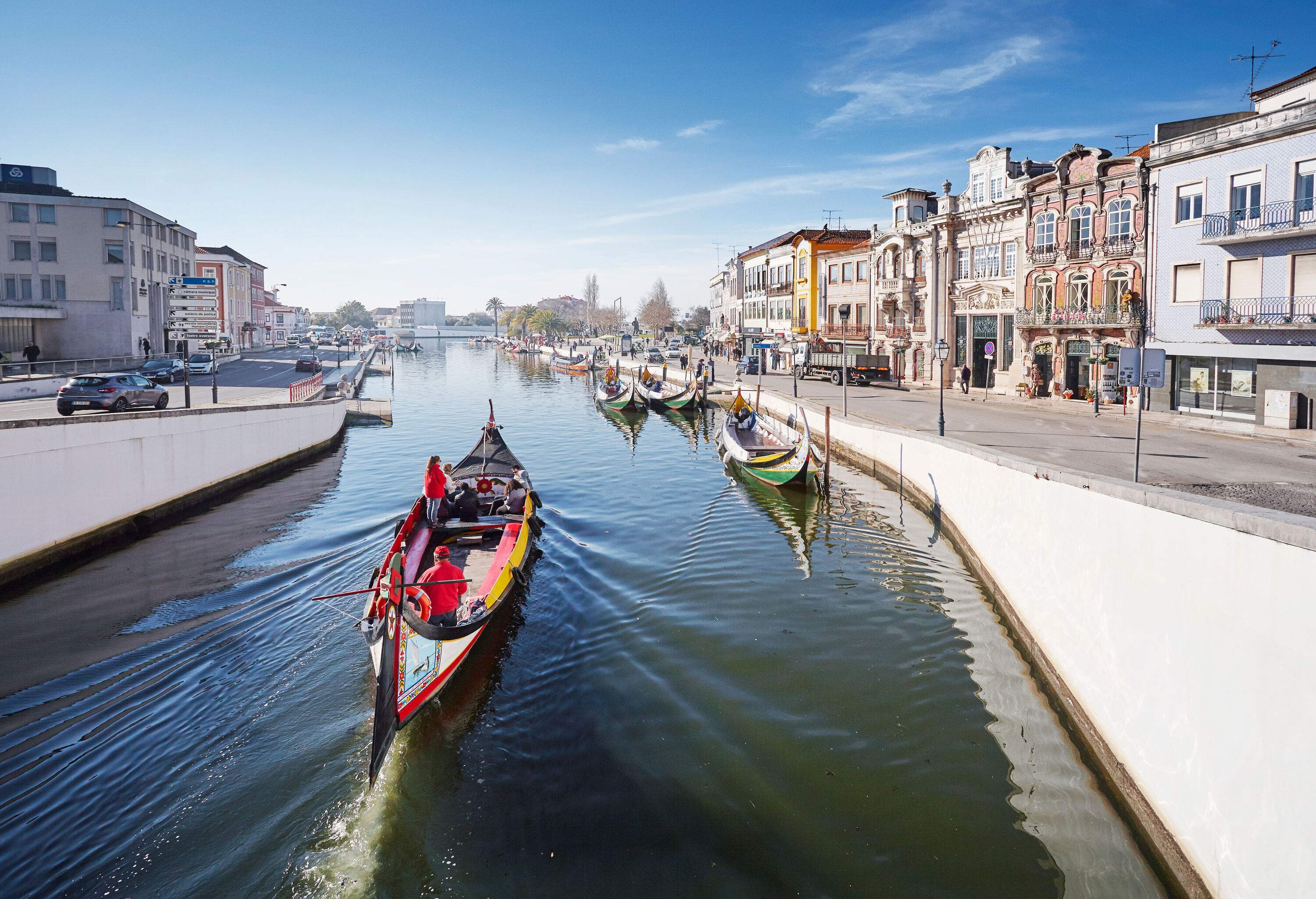 A boat sailing in the middle of a canal lined with docked boats bordered by colourful buildings.