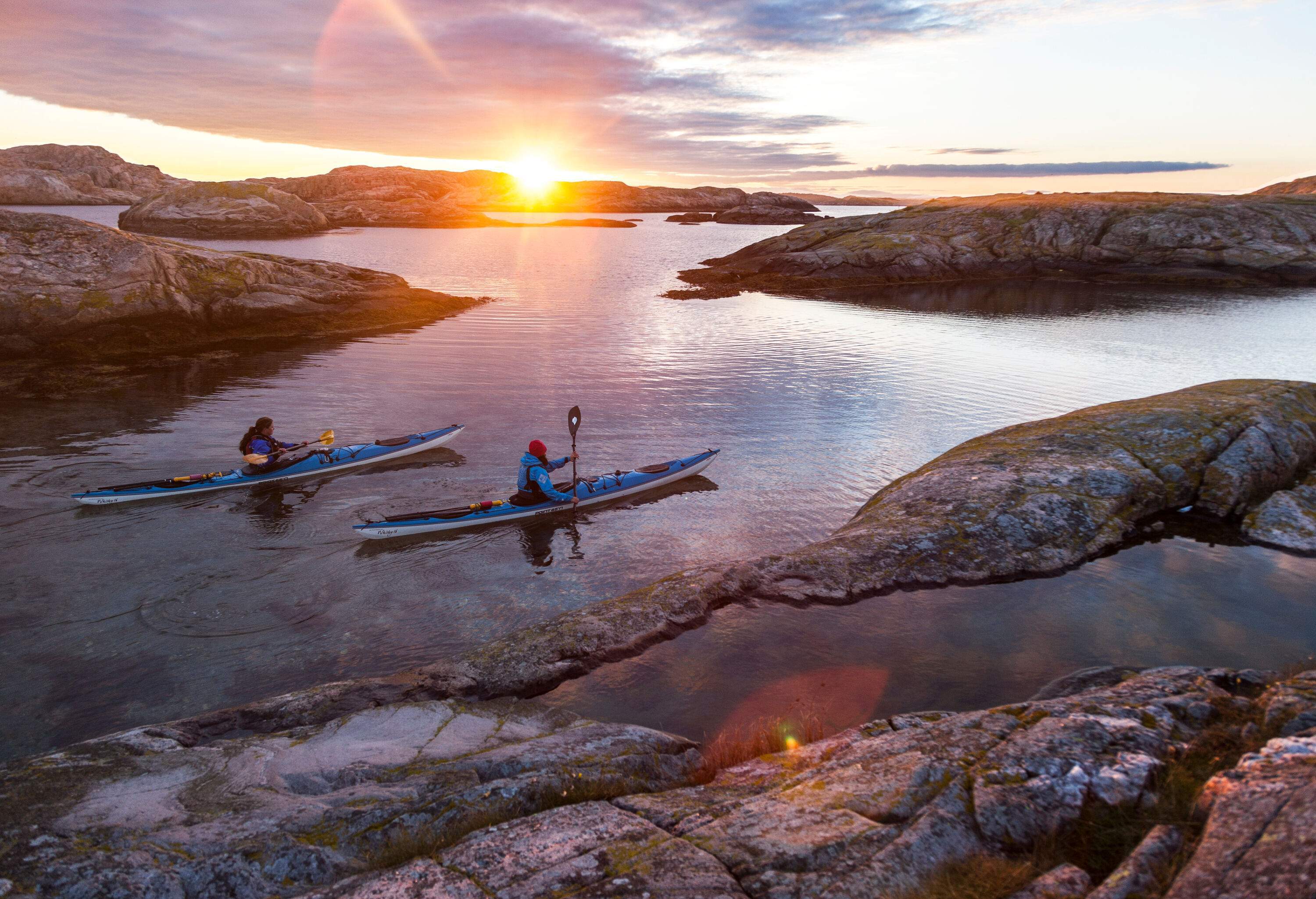 two people paddeling in kayaks in the swedish archipelago during the sunrise