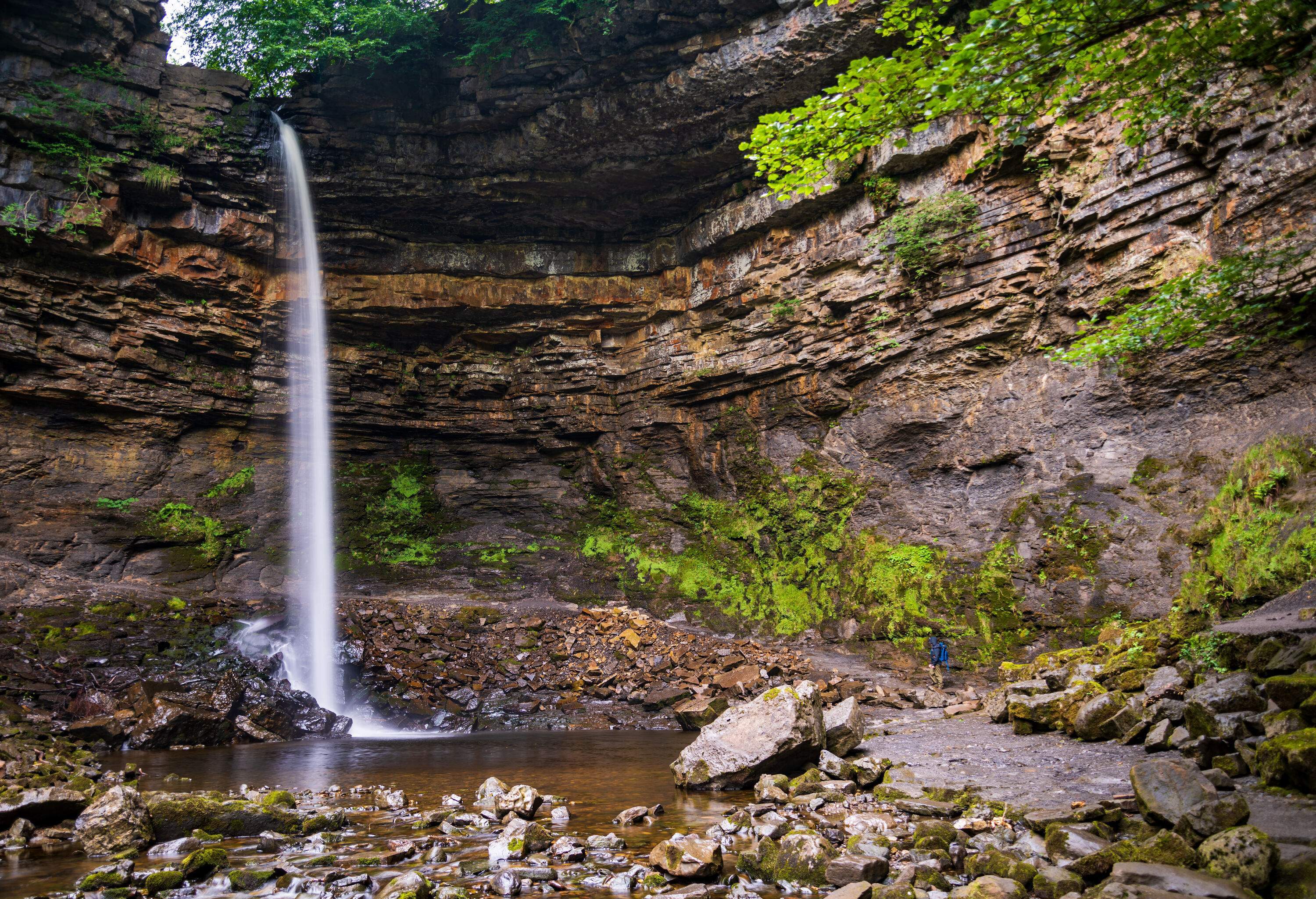 A waterfall falls straight down to the ground below, which is surrounded by cliff edges, rocks, and some plants.