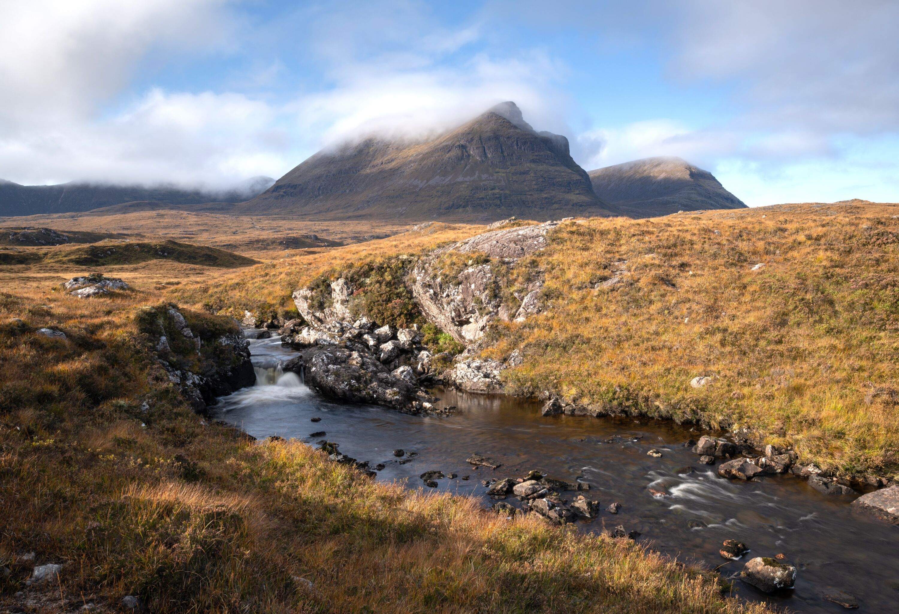 View of a small river in the Highlands with a mountain covered in clouds in the background