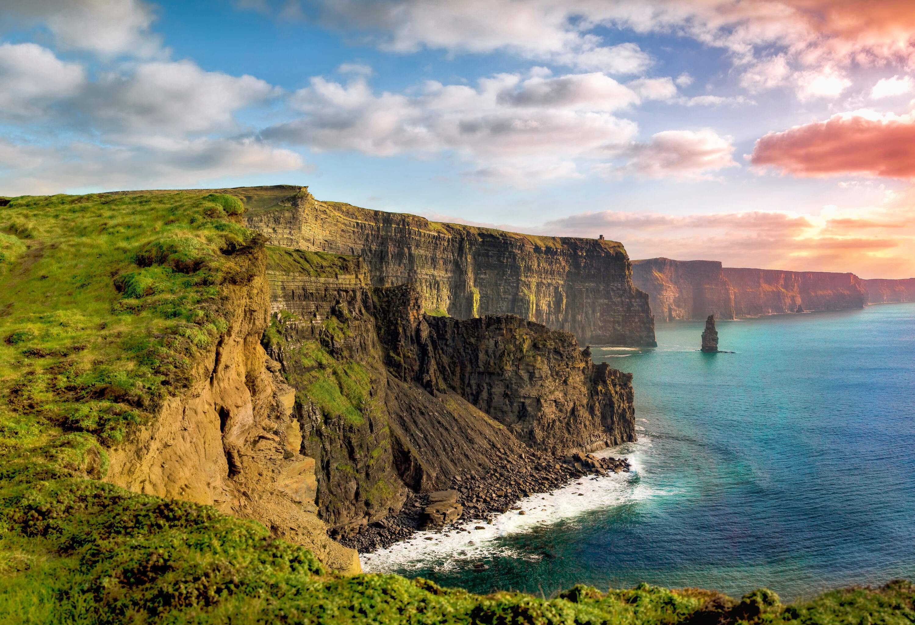 A woman and her dog standing on the grassy plateau on top of the Cliffs of Moher.