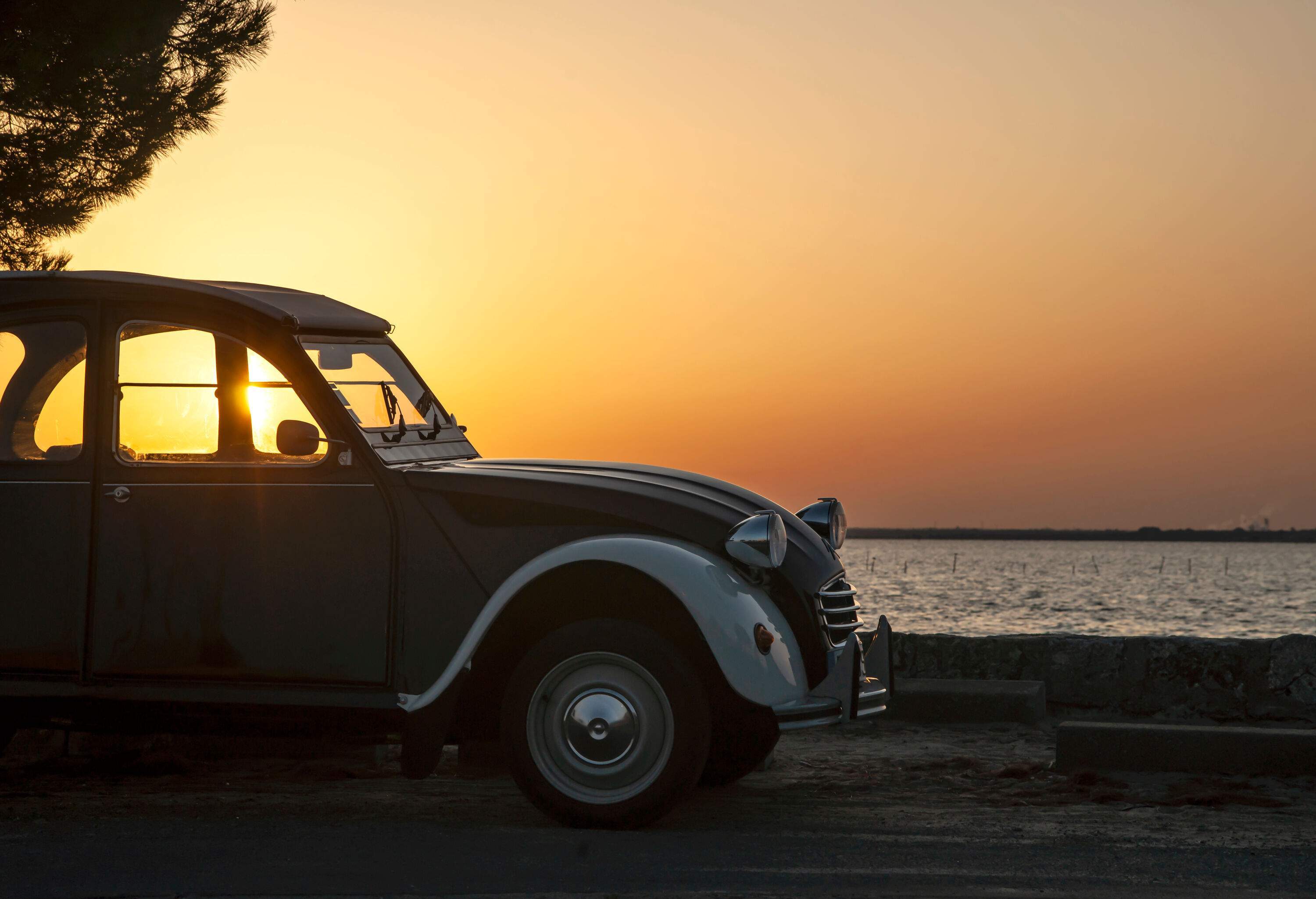 Silhouette of a vintage car parked on a beach against the backdrop of a beautiful sunset and orange skies.
