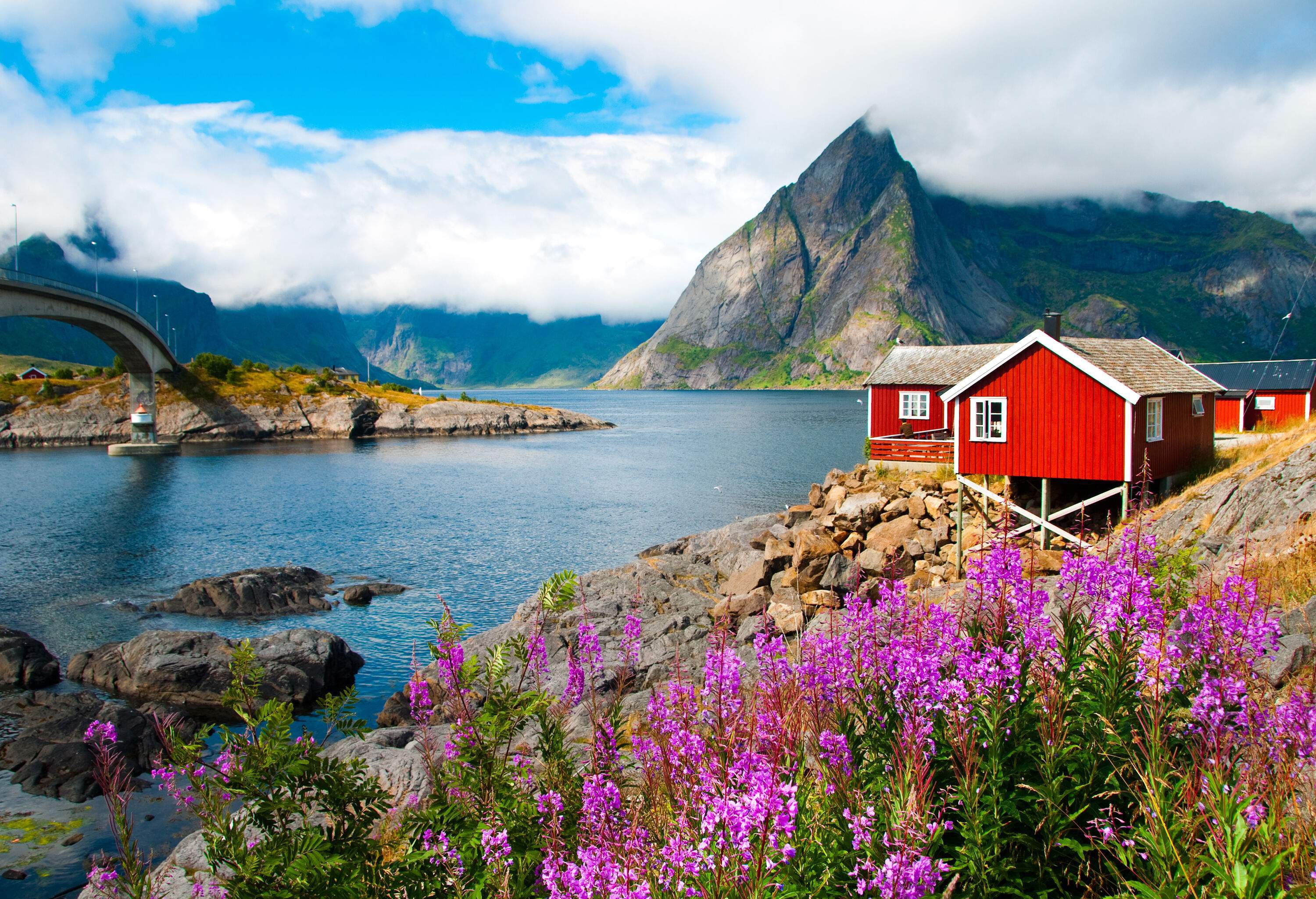 Red wooden houses nestled alongside a river that flows through the steep mountains and spanned by a bridge.