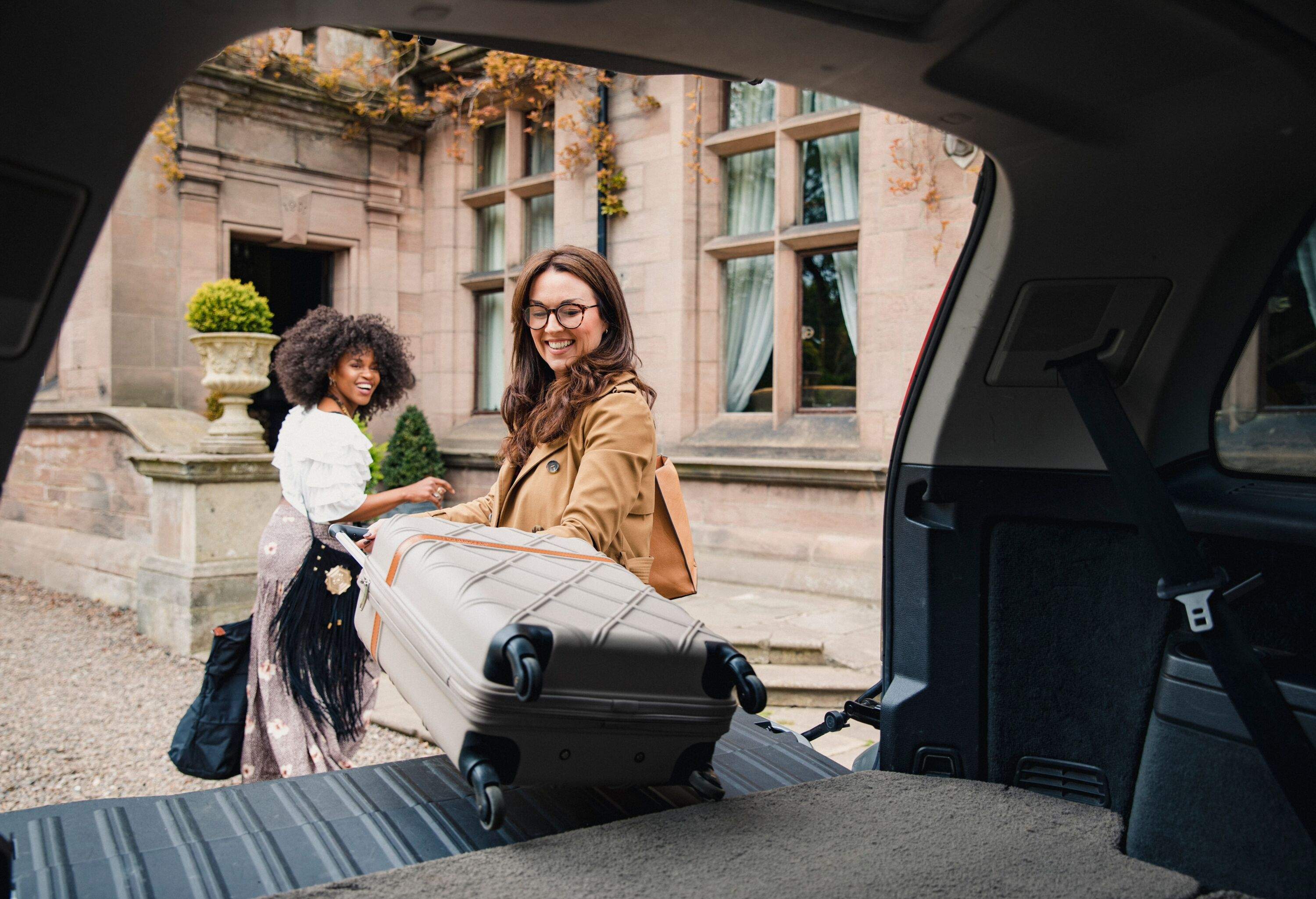 Two friends arrive at a luxury hotel where they are unloading their suitcases from their car trunk.