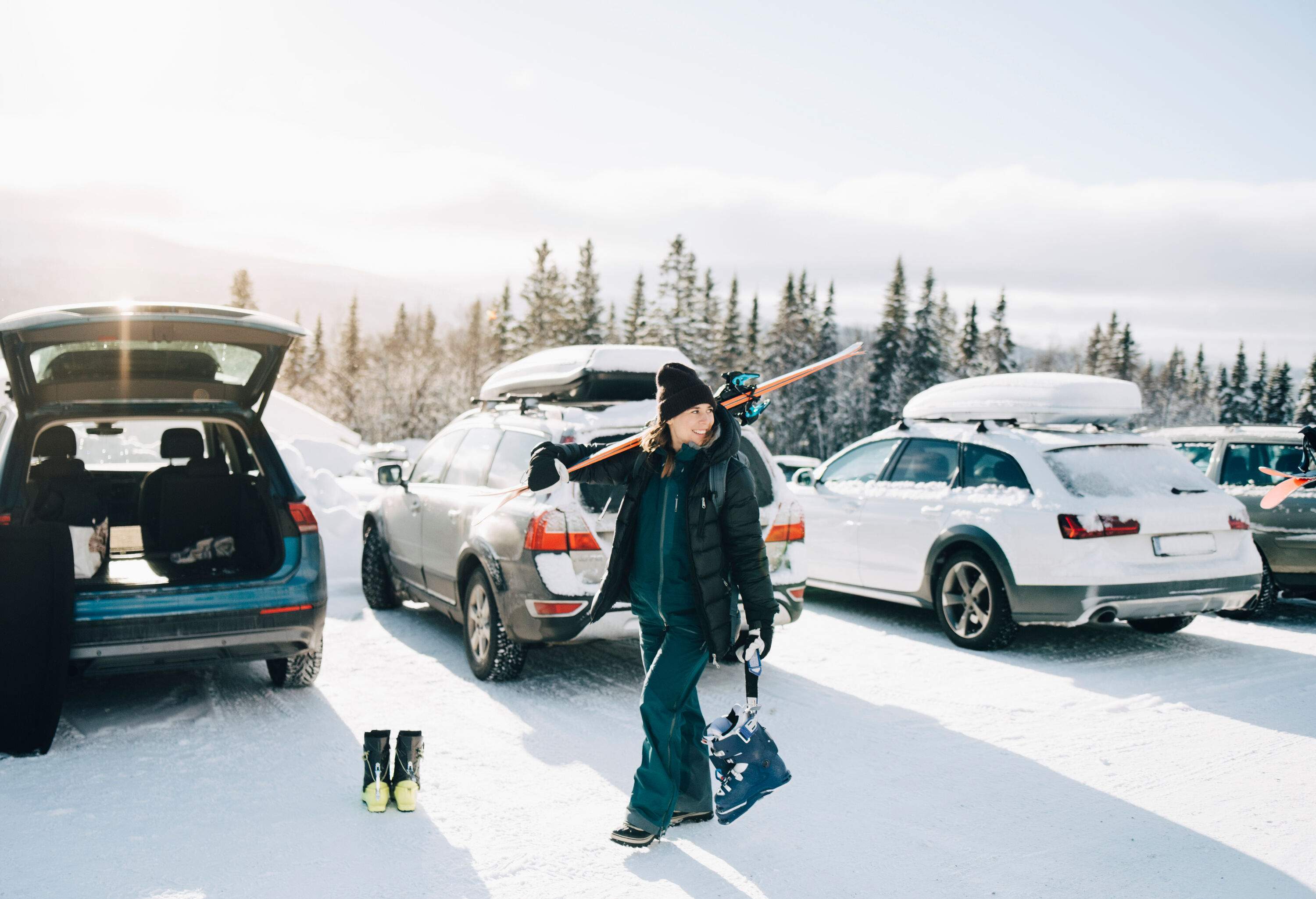 A smiling woman wearing a winter coat, scarf, and gloves walks on snow in a parking lot.