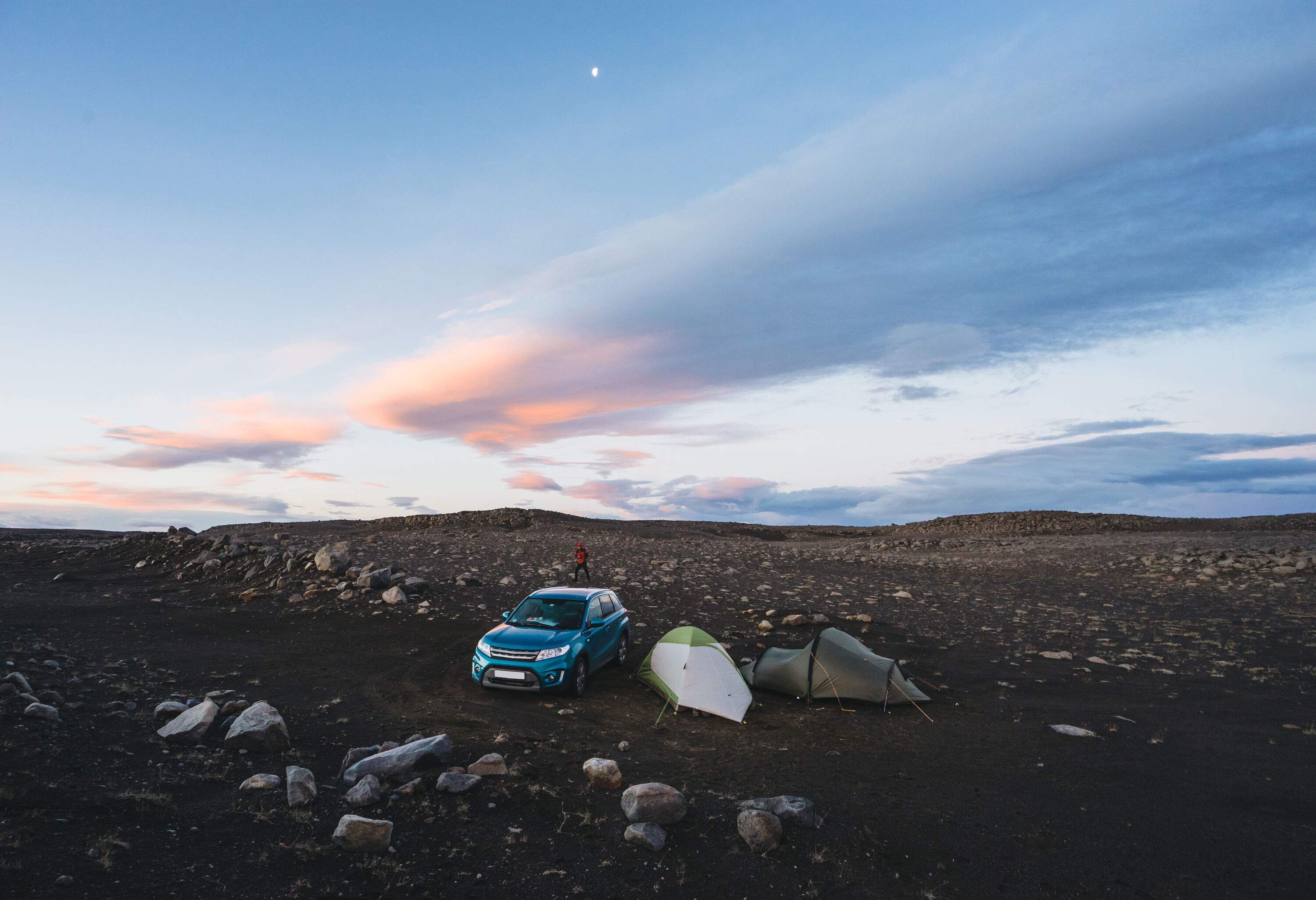 Navy blue car parked next to two tents on a rocky terrain.