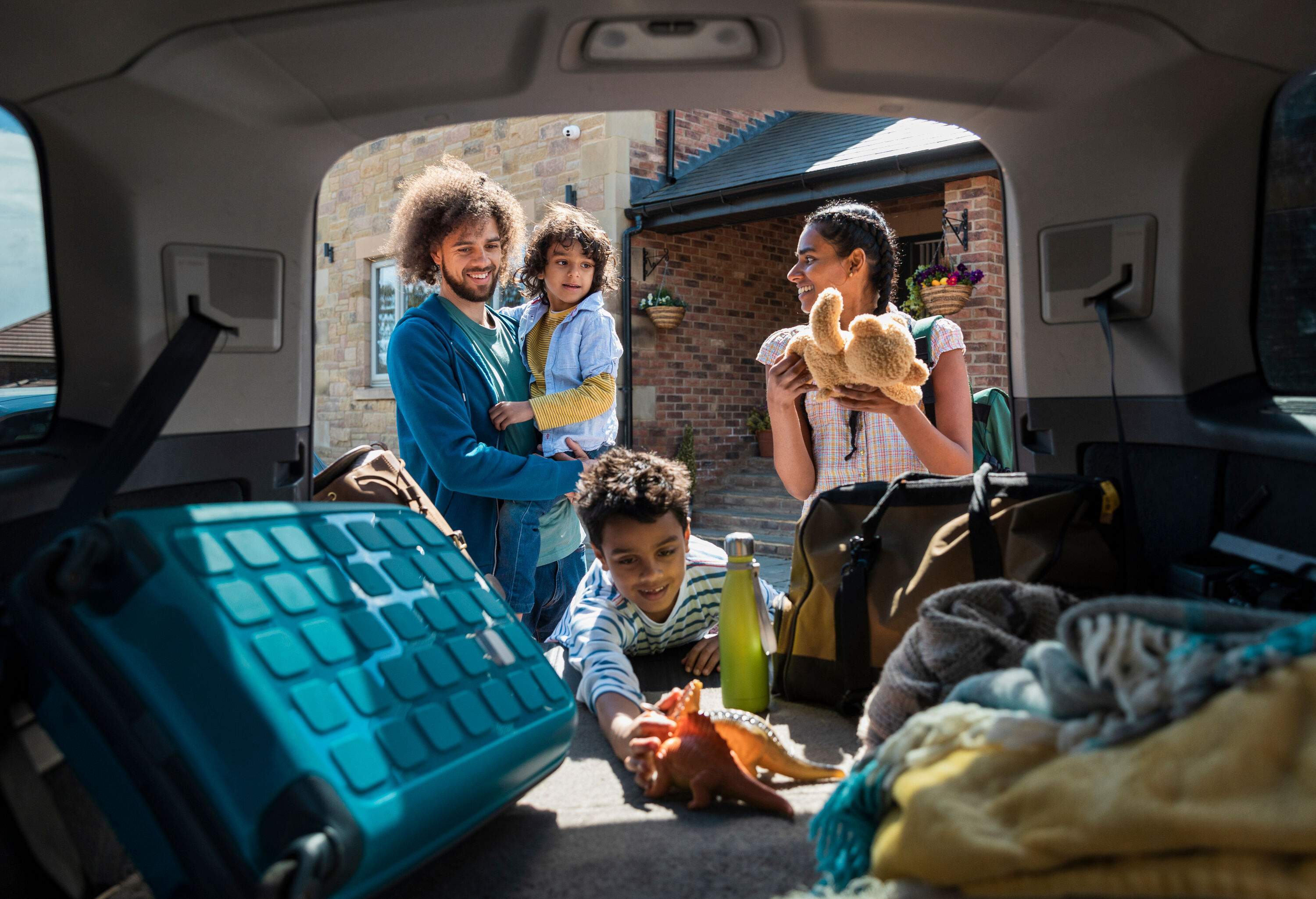 A family of four takes their bags and the kid's toys from the back of their car.