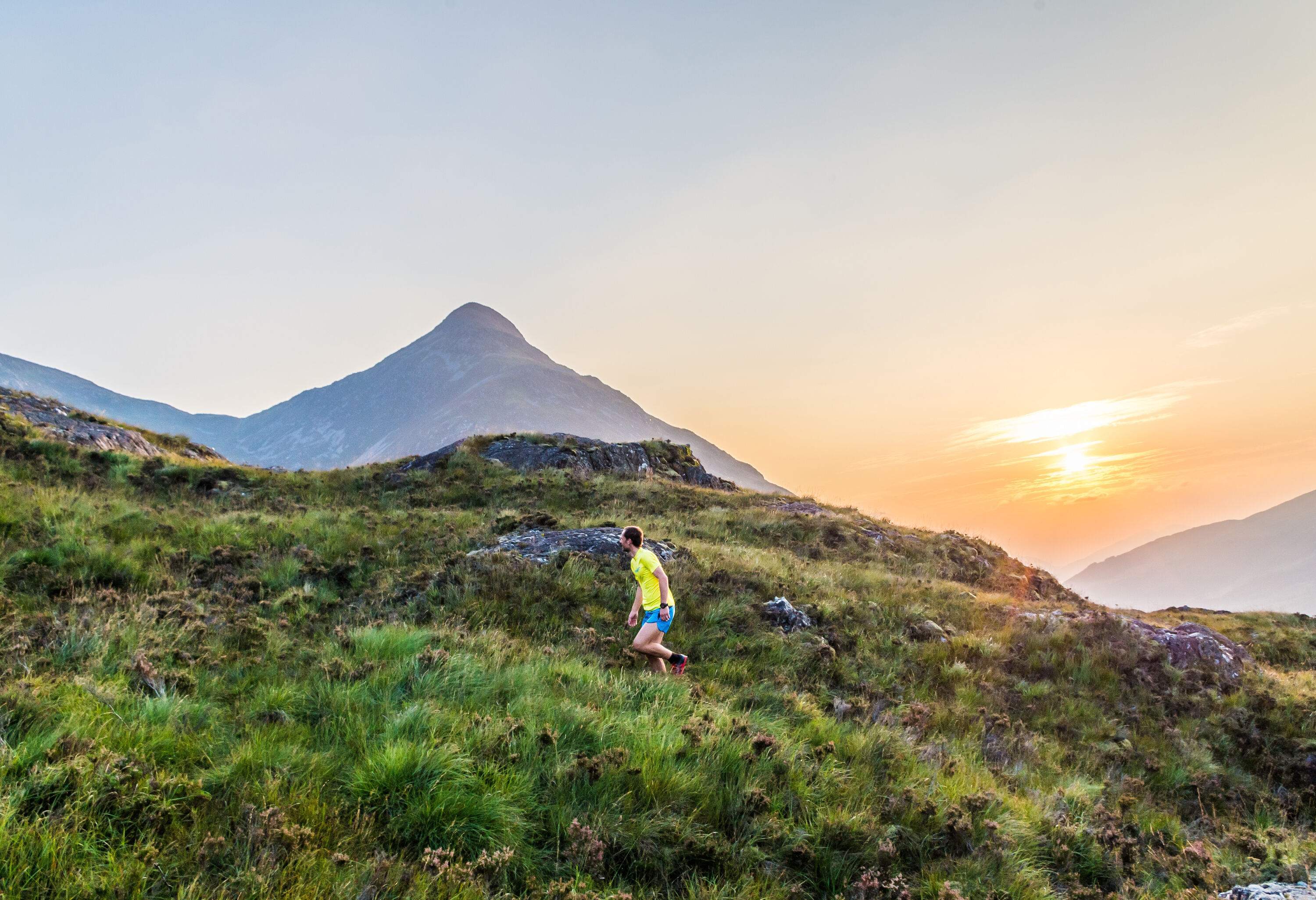 A man in a yellow shirt running on a less-trodden trail at sunset.