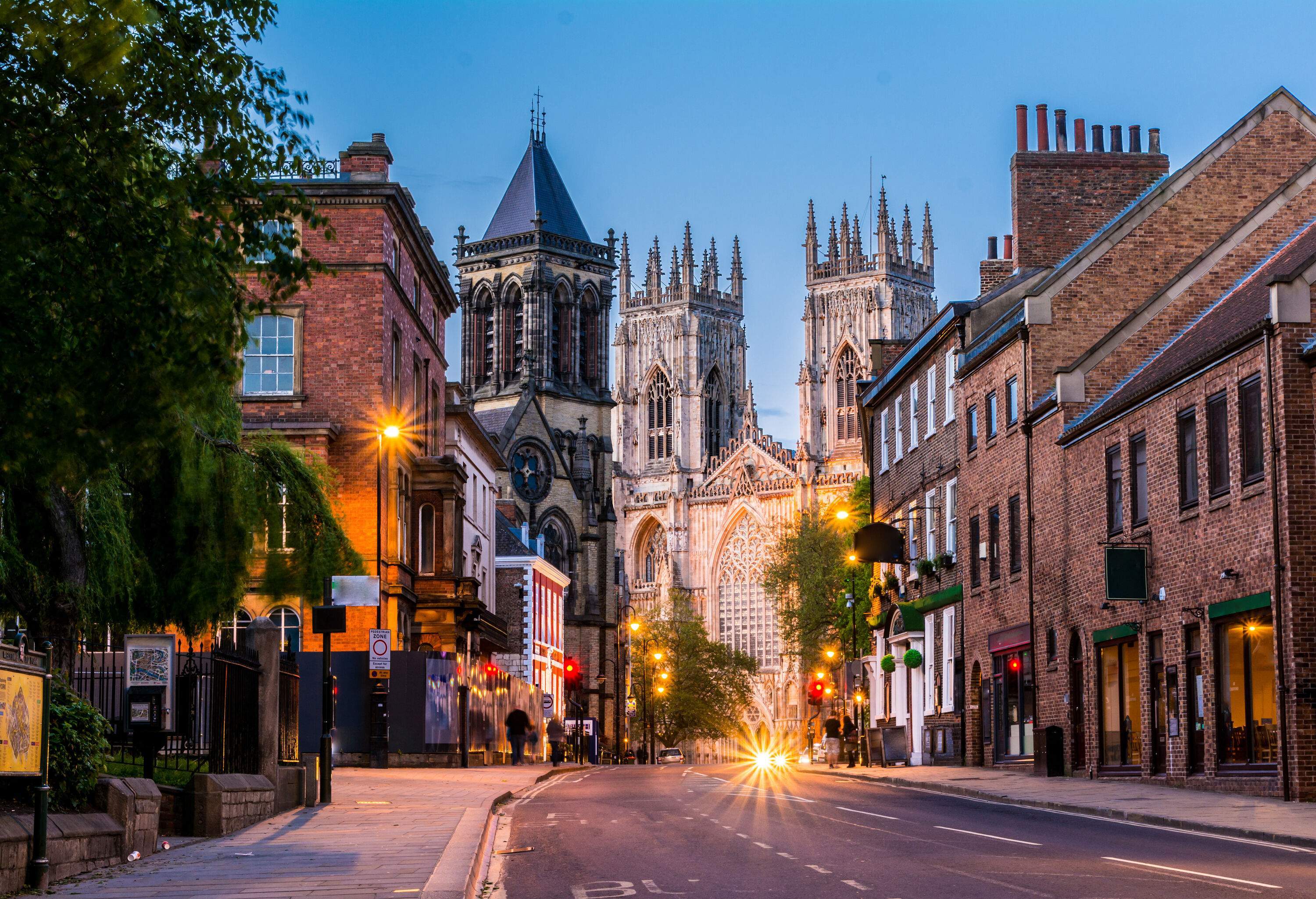 The York Minster cathedral can be seen in the distance, along with a street lined with brick houses and illuminated lampposts.