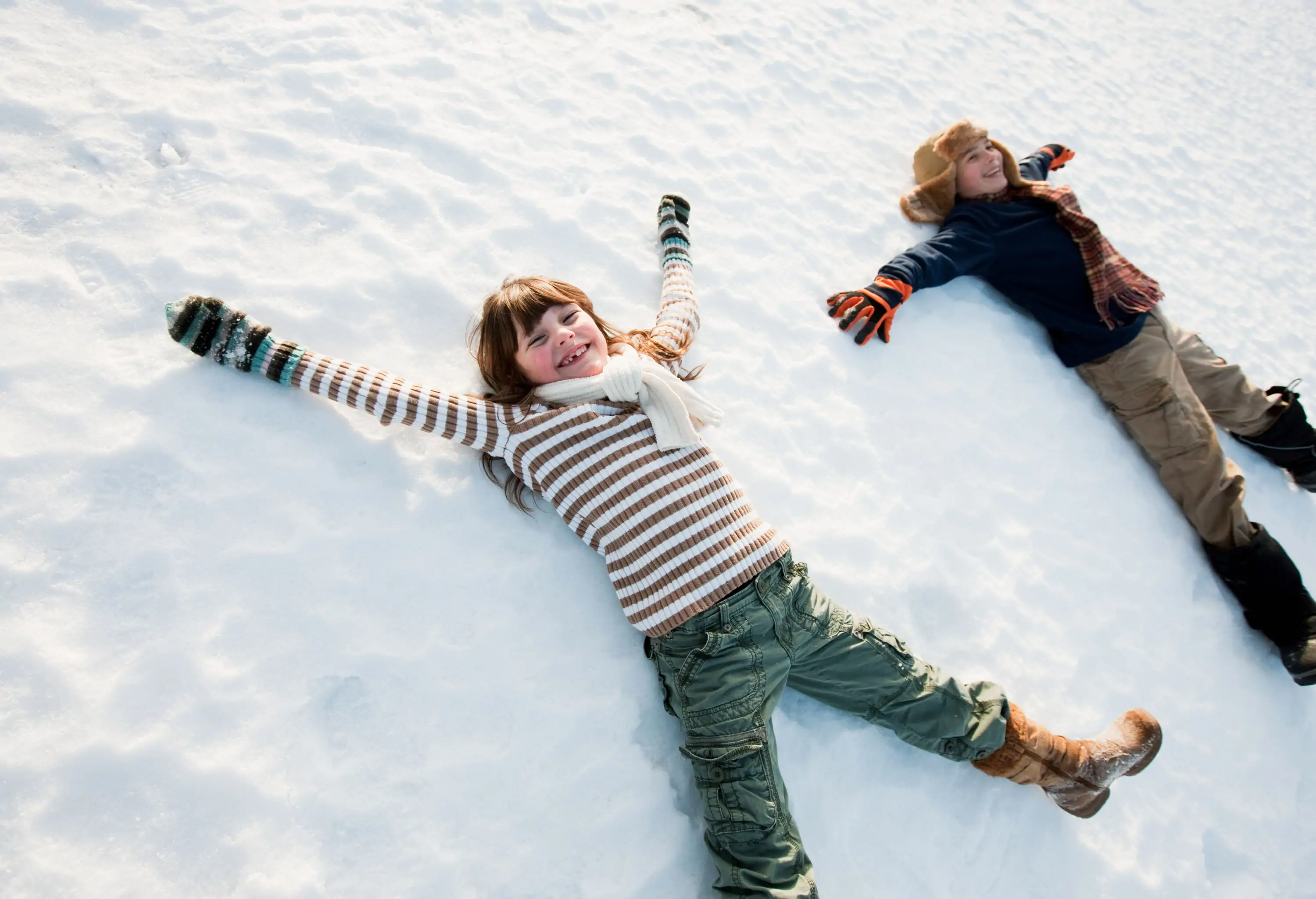 Two children lying in the snow-covered land make snow angel figures.