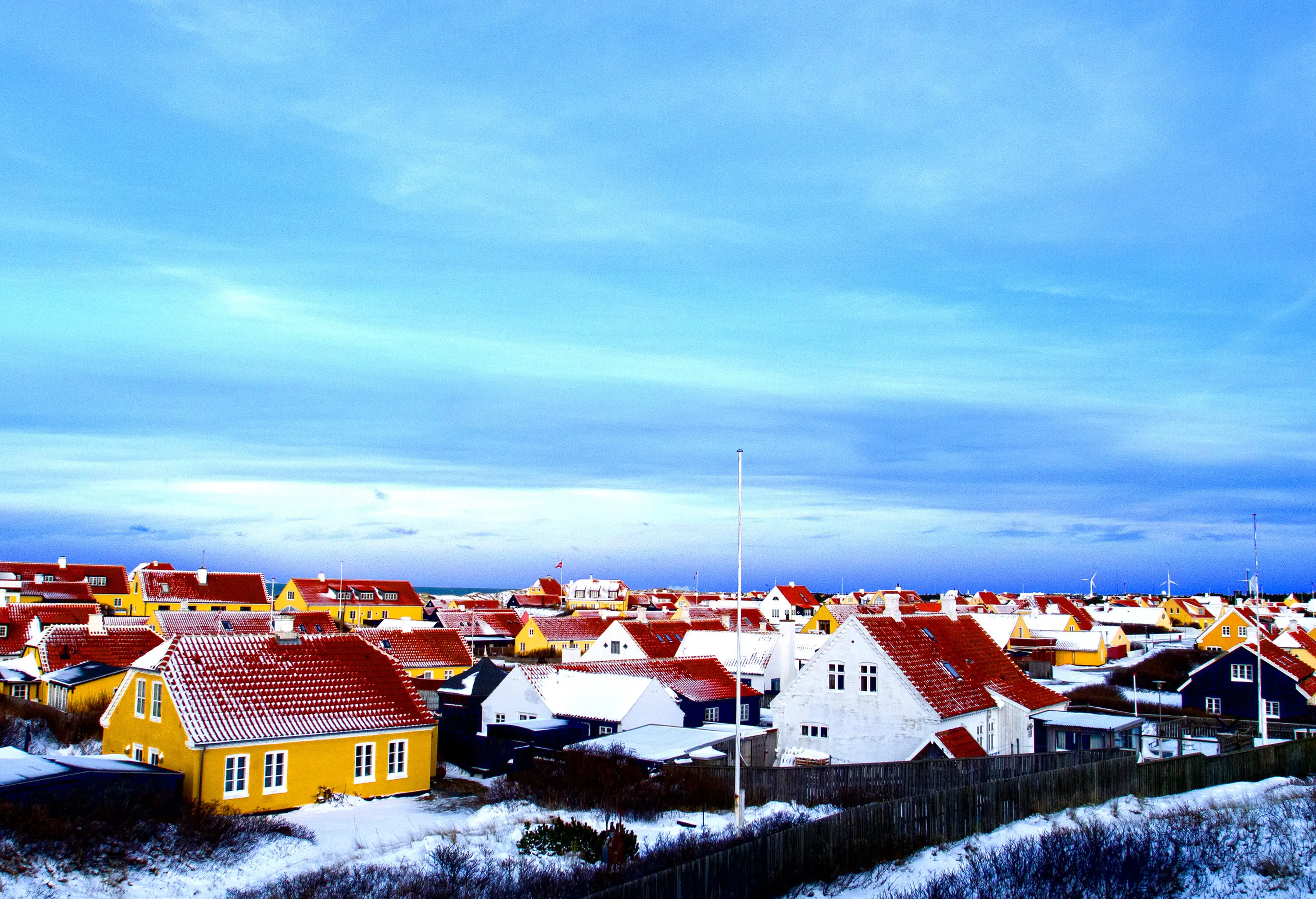 Red tiled roof houses with yellow and white plastered walls surrounded by black wooden fences.