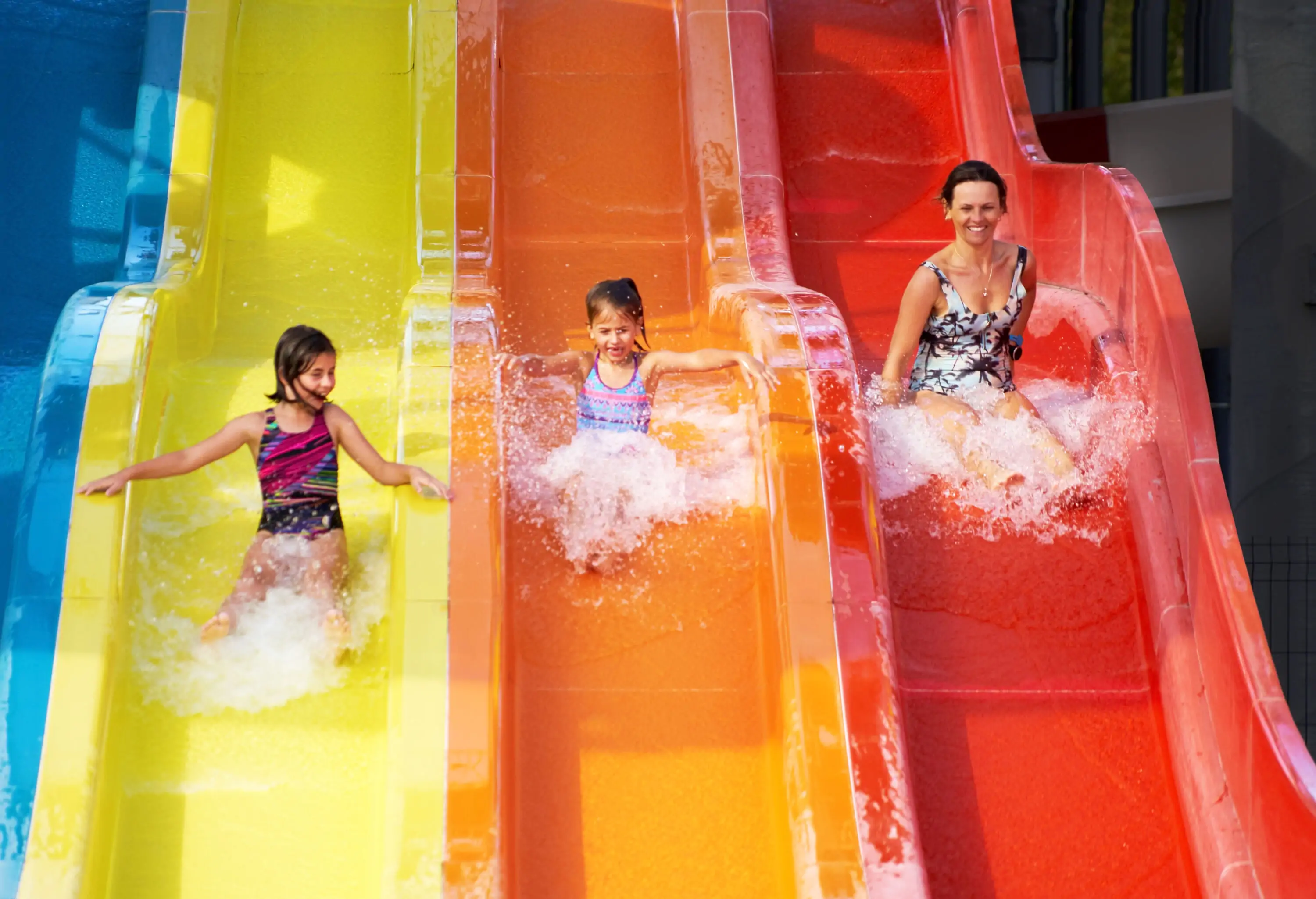 Three people go down a yellow, orange, and red water slide.