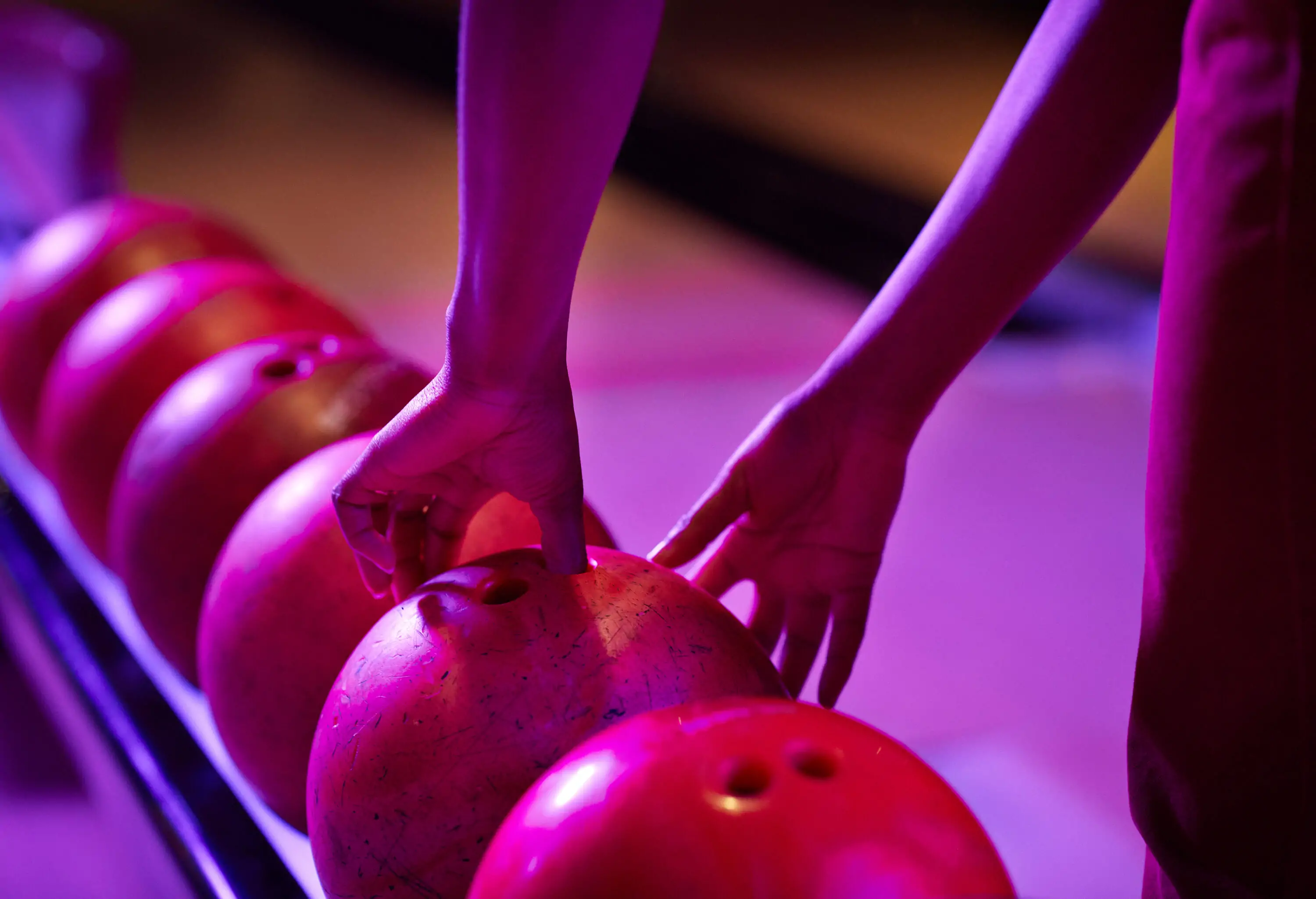 A woman inserting her fingers into the holes of a bowling ball to pick it off the resting rail.