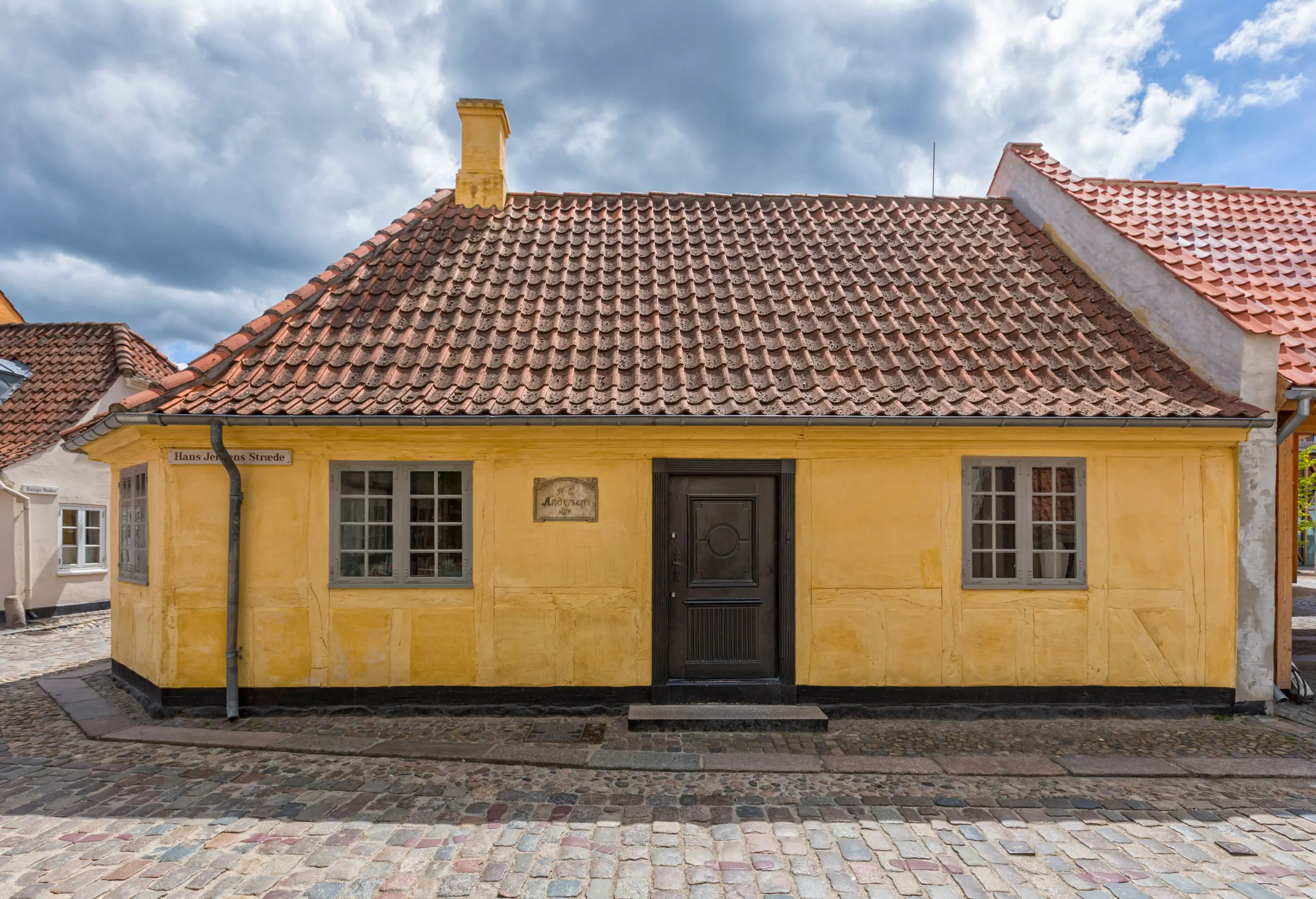 A yellow house with wooden door, glass windows, and tiled roof along a cobblestone street.