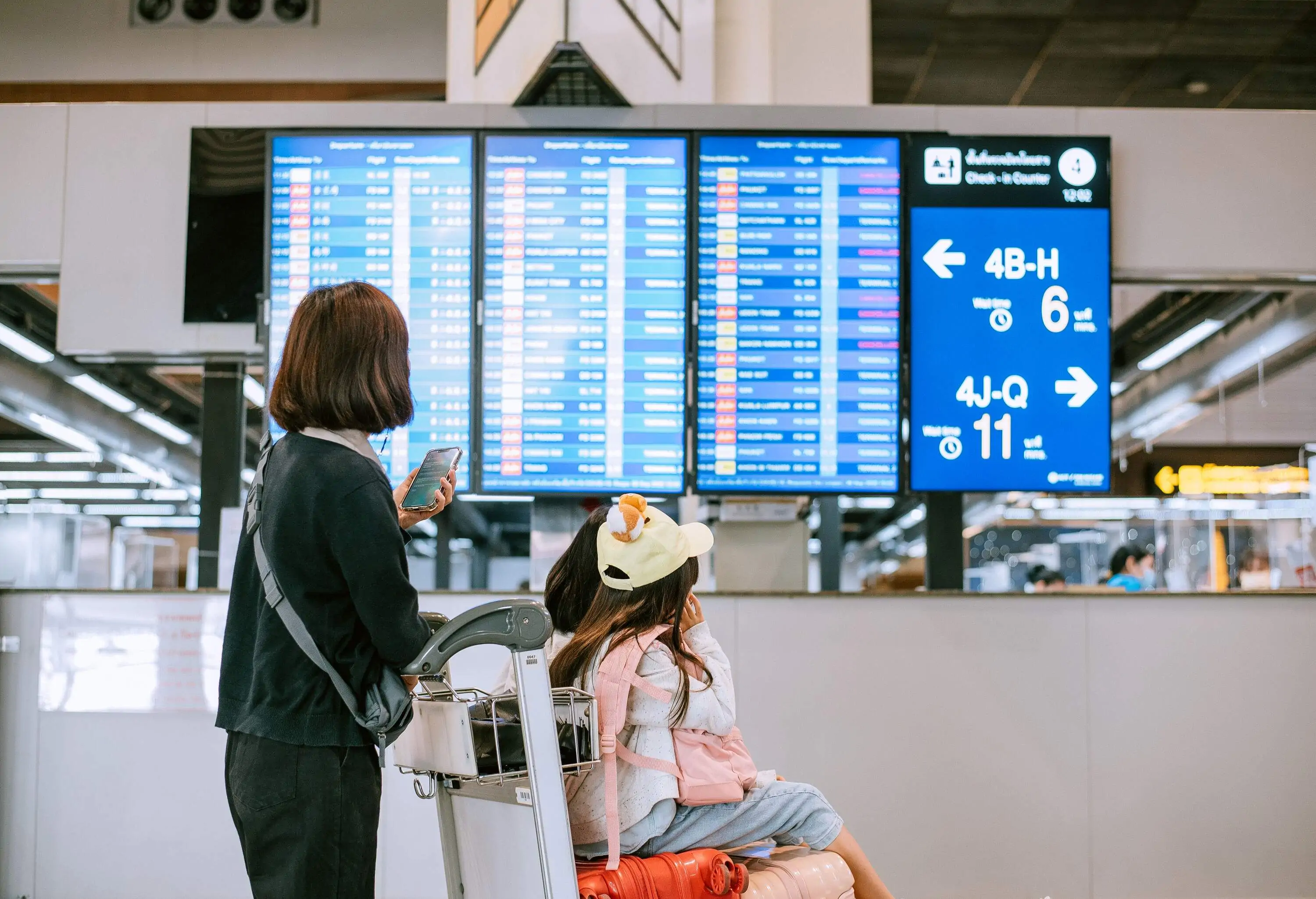 Mother and daughter at airport with trolley looking at departures screen