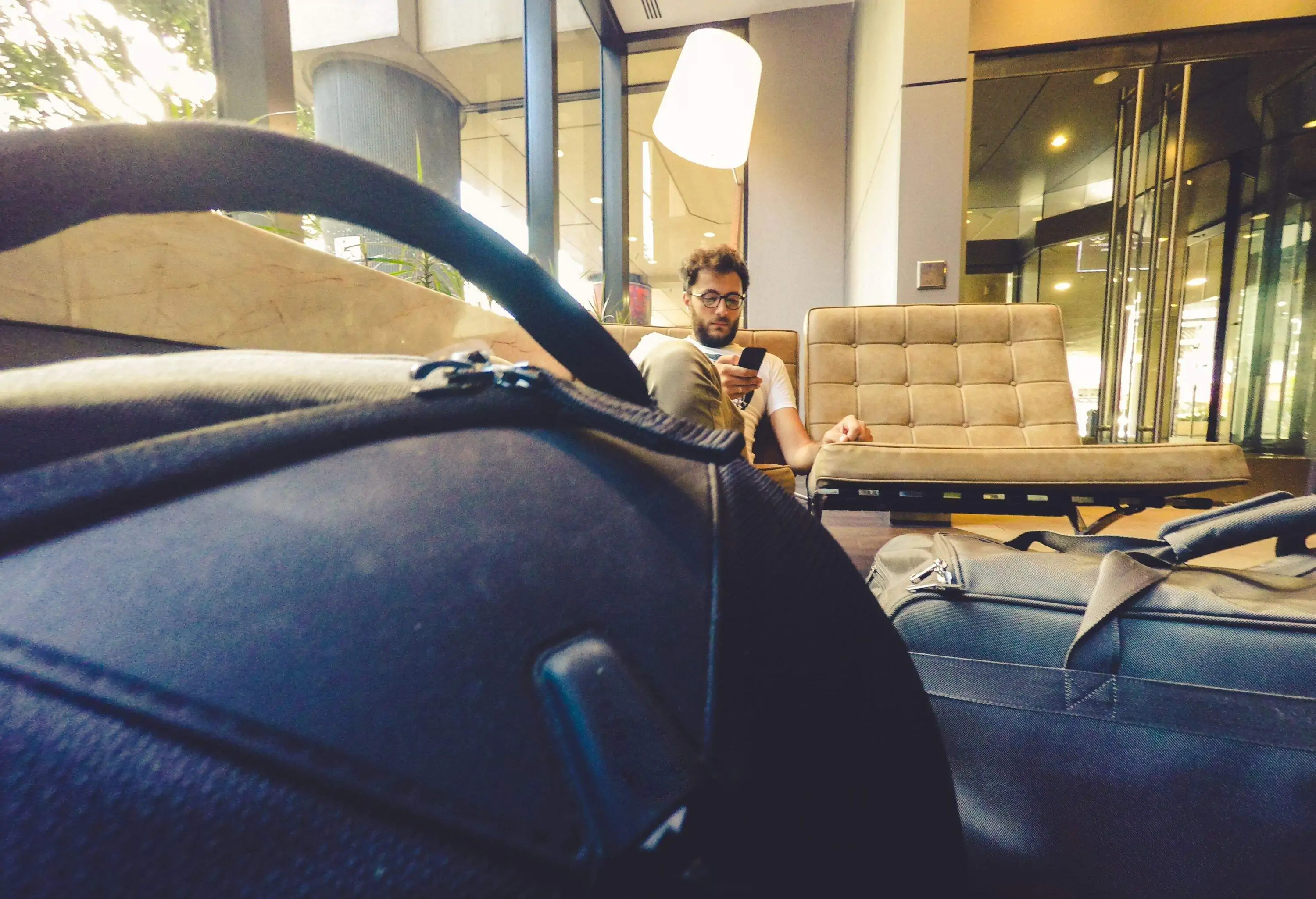 Man using mobile phone while waiting for flight at airport lounge, luggage in foreground