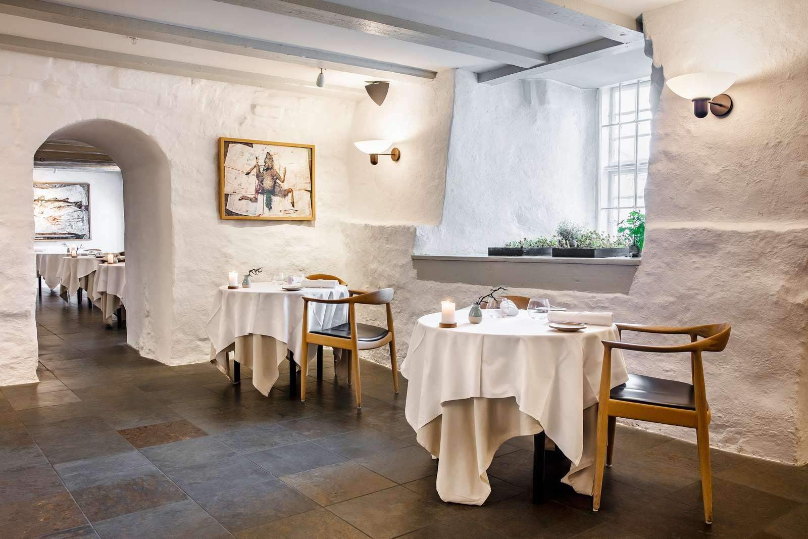 Interior view of restaurant with two set tables by a window, white walls and low ceilings in historical building