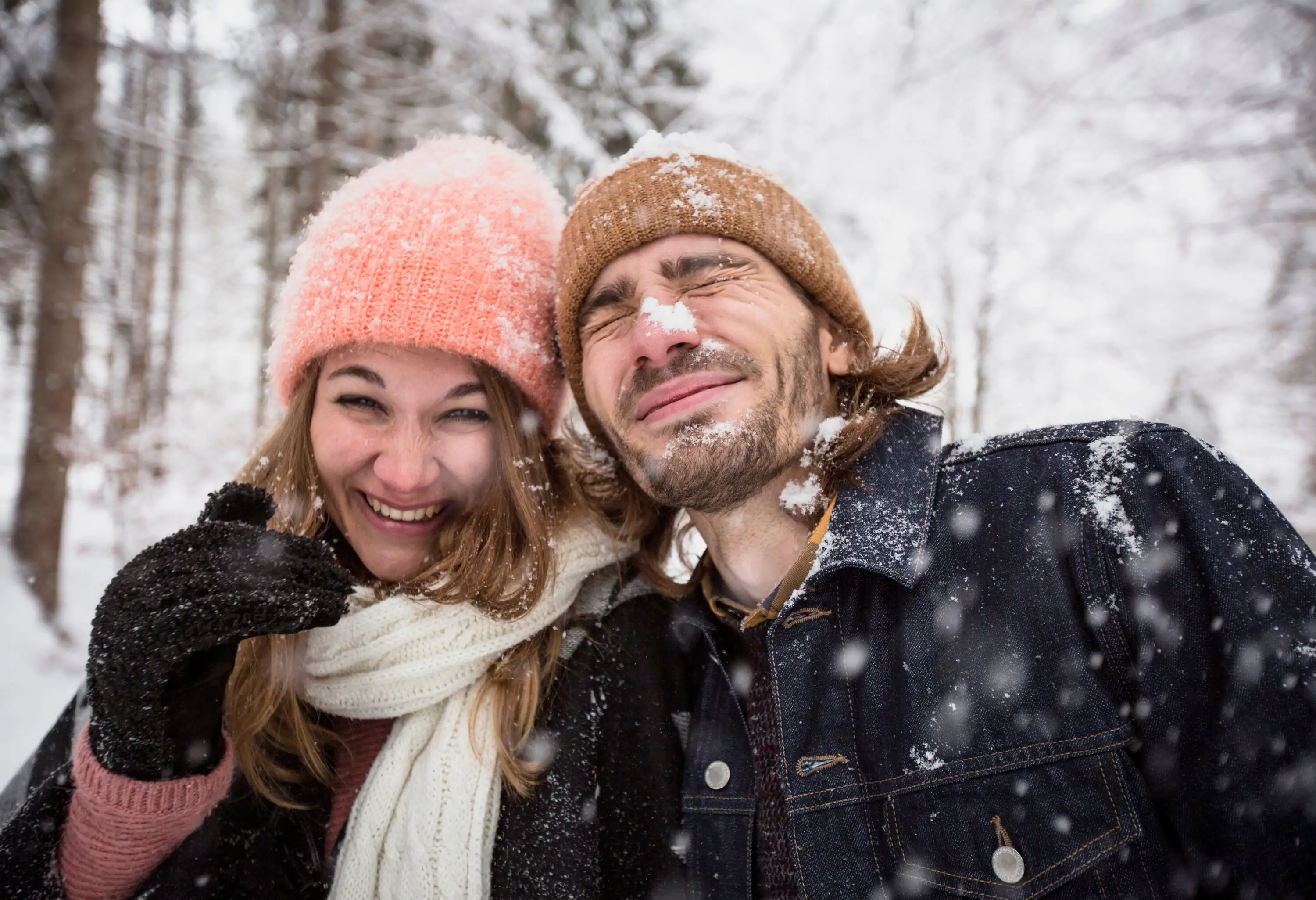 A lovely couple in thick clothes and beanies having fun outdoors with the falling snowflakes.