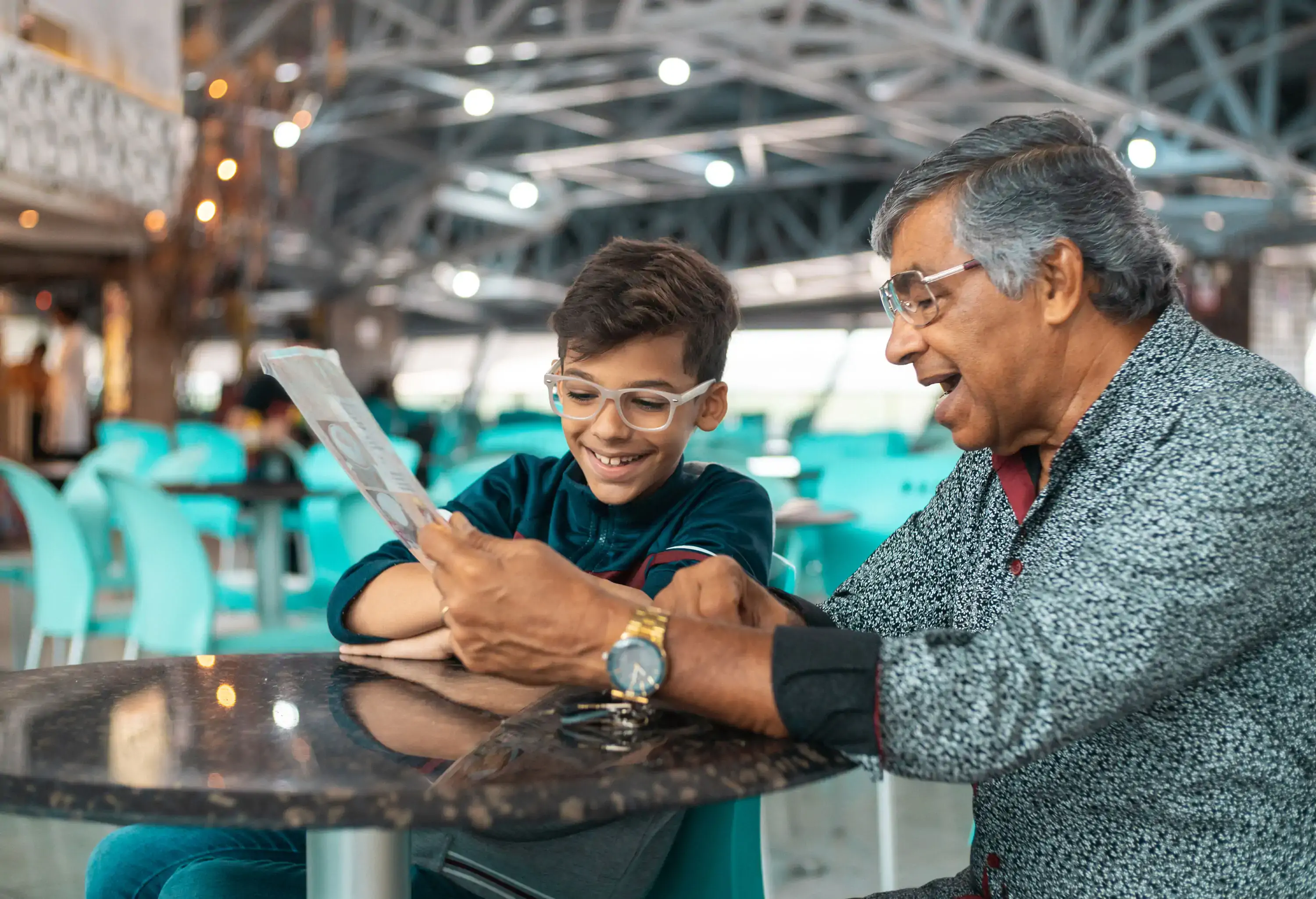 Grandfather and nephew both wearing glasses and smiling reading food menu at airport cafe