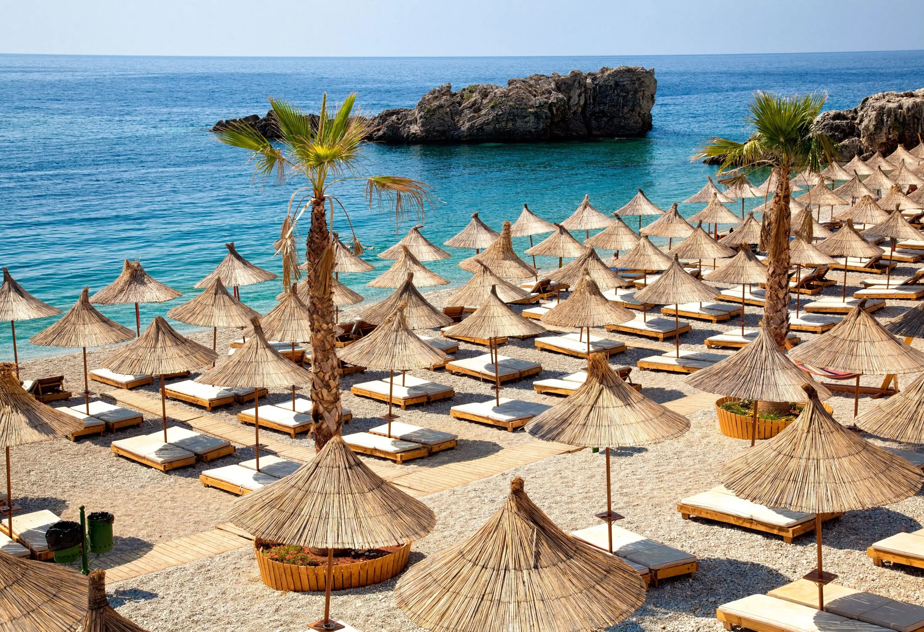 A beach with rows of sunbeds under thatched umbrellas.