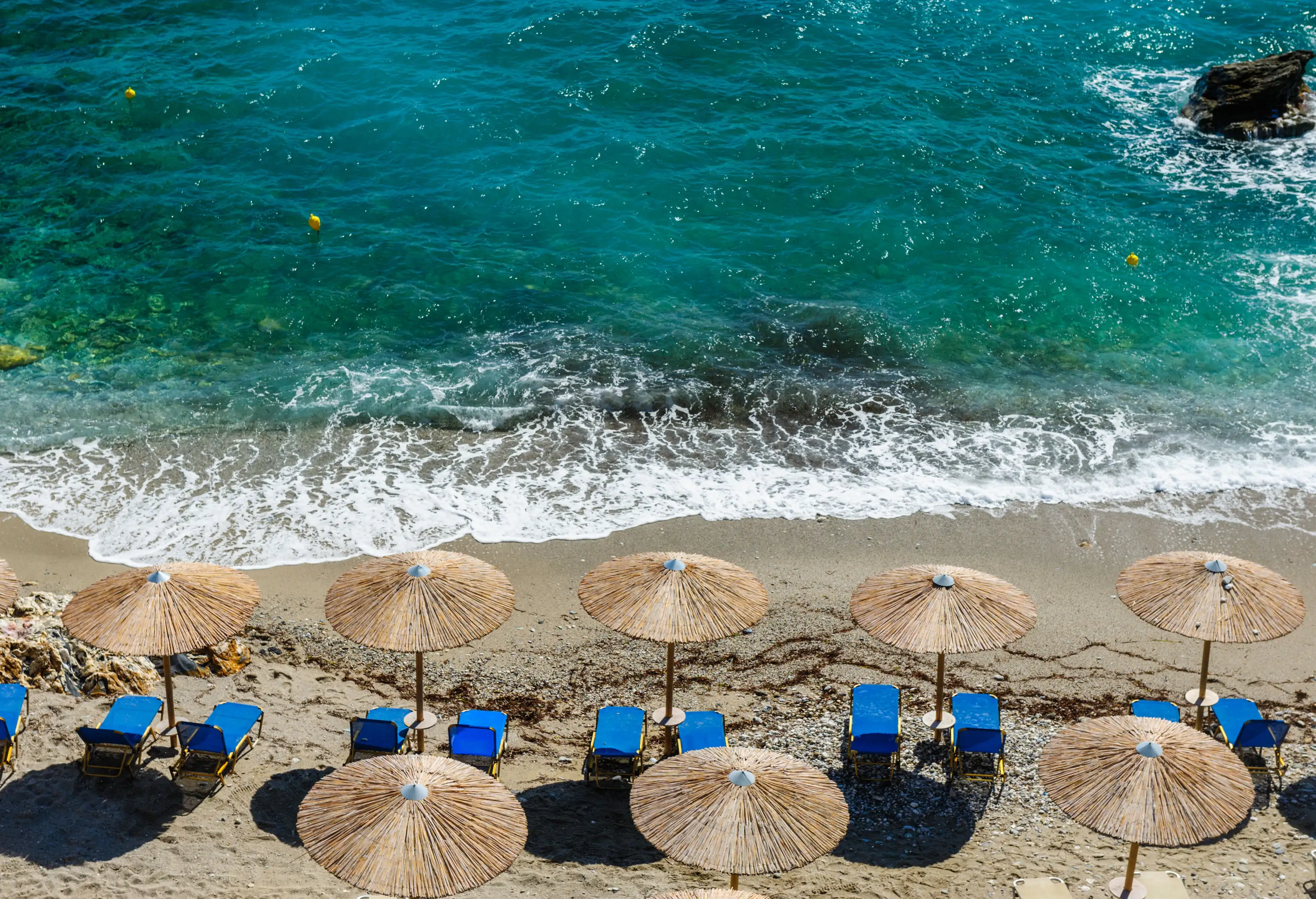 Waves crashing on the beach across from the loungers and thatched umbrellas.