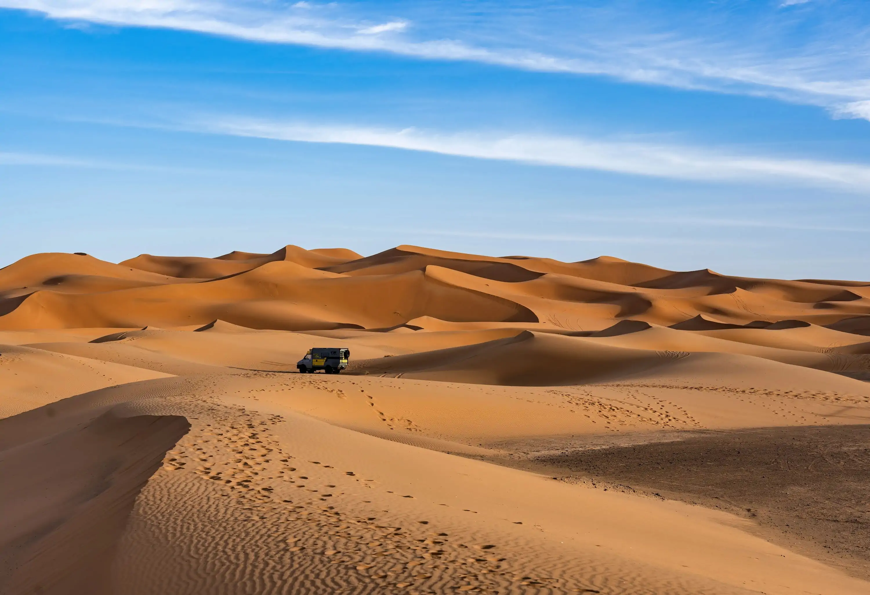 n off-road vehicle navigates the sweeping dunes of the Sahara under a wide blue sky, showcasing the allure of adventure travel.