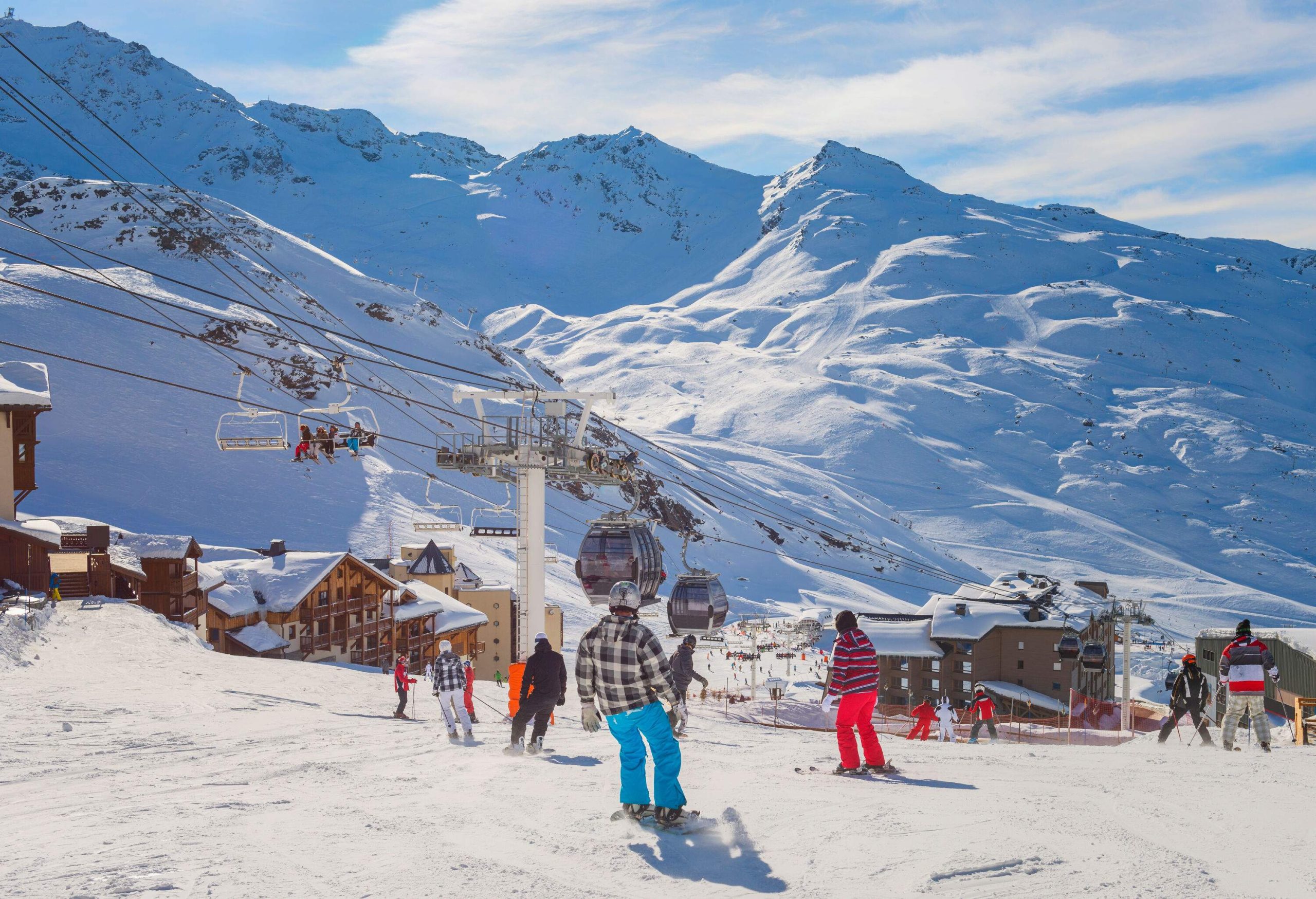 Crowd of skiers descending a snow hill with views of hanging chairlifts and cable cars above a ski village.