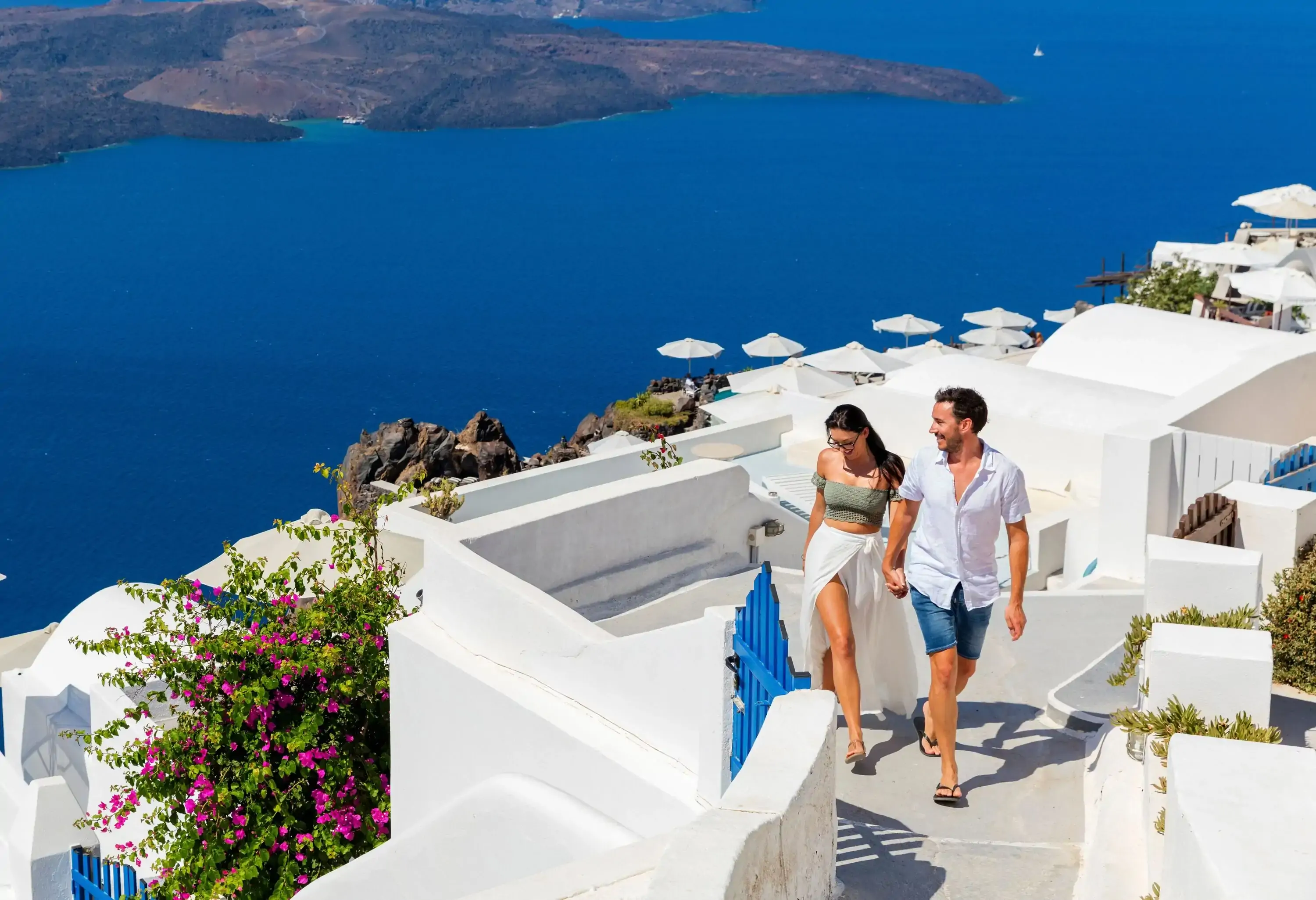 A sweet couple holding hands while walking up the steps of a white village by the ocean.