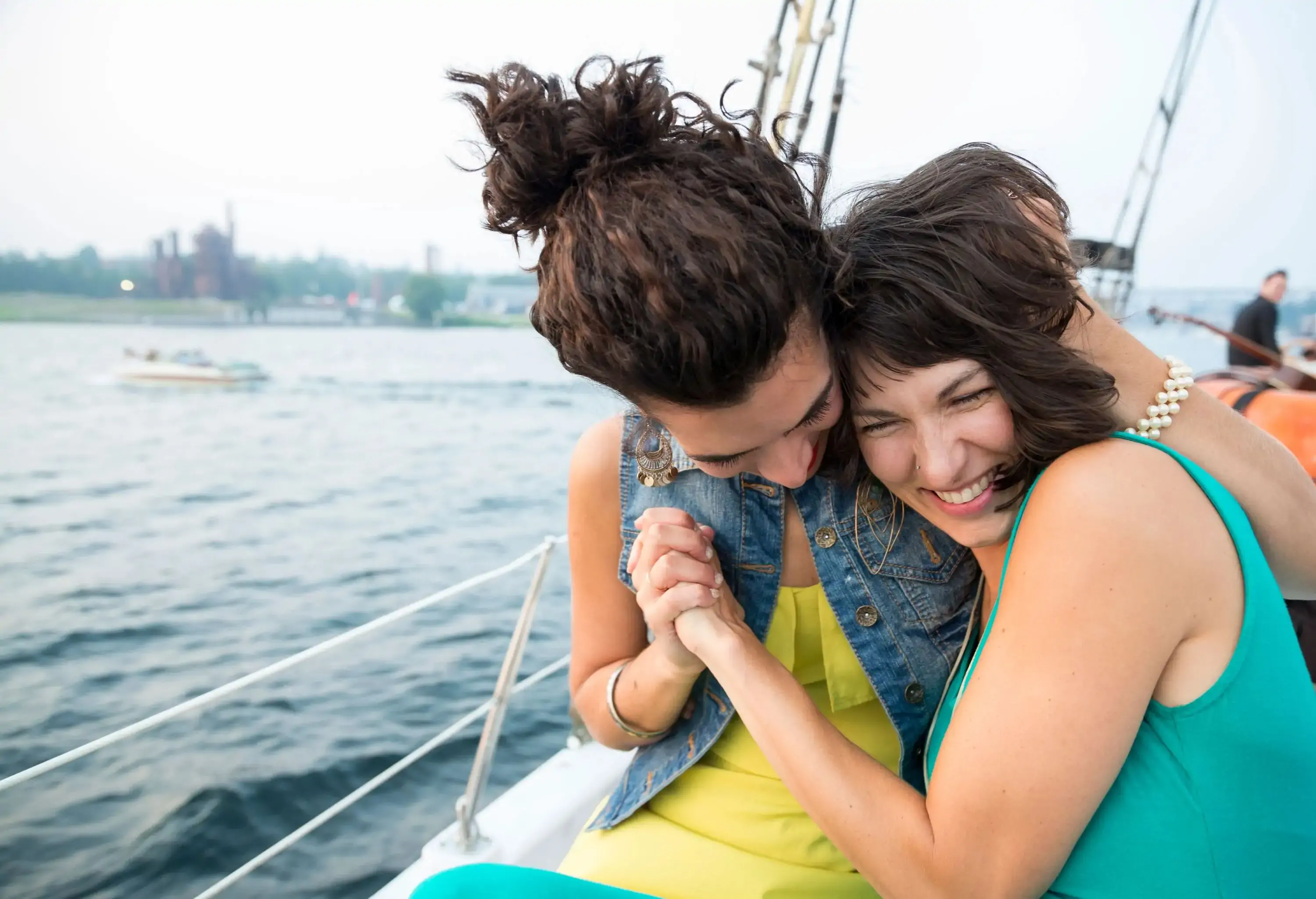 A lesbian couple hugs and laughs on a sailboat.