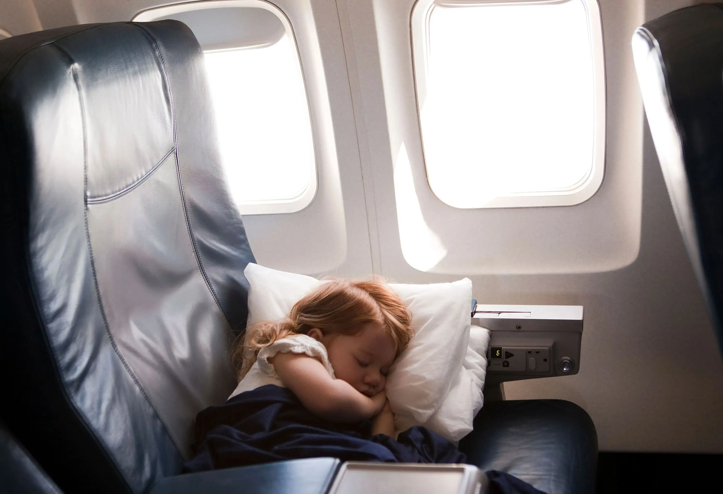 A child sleeping on a plane next to a window