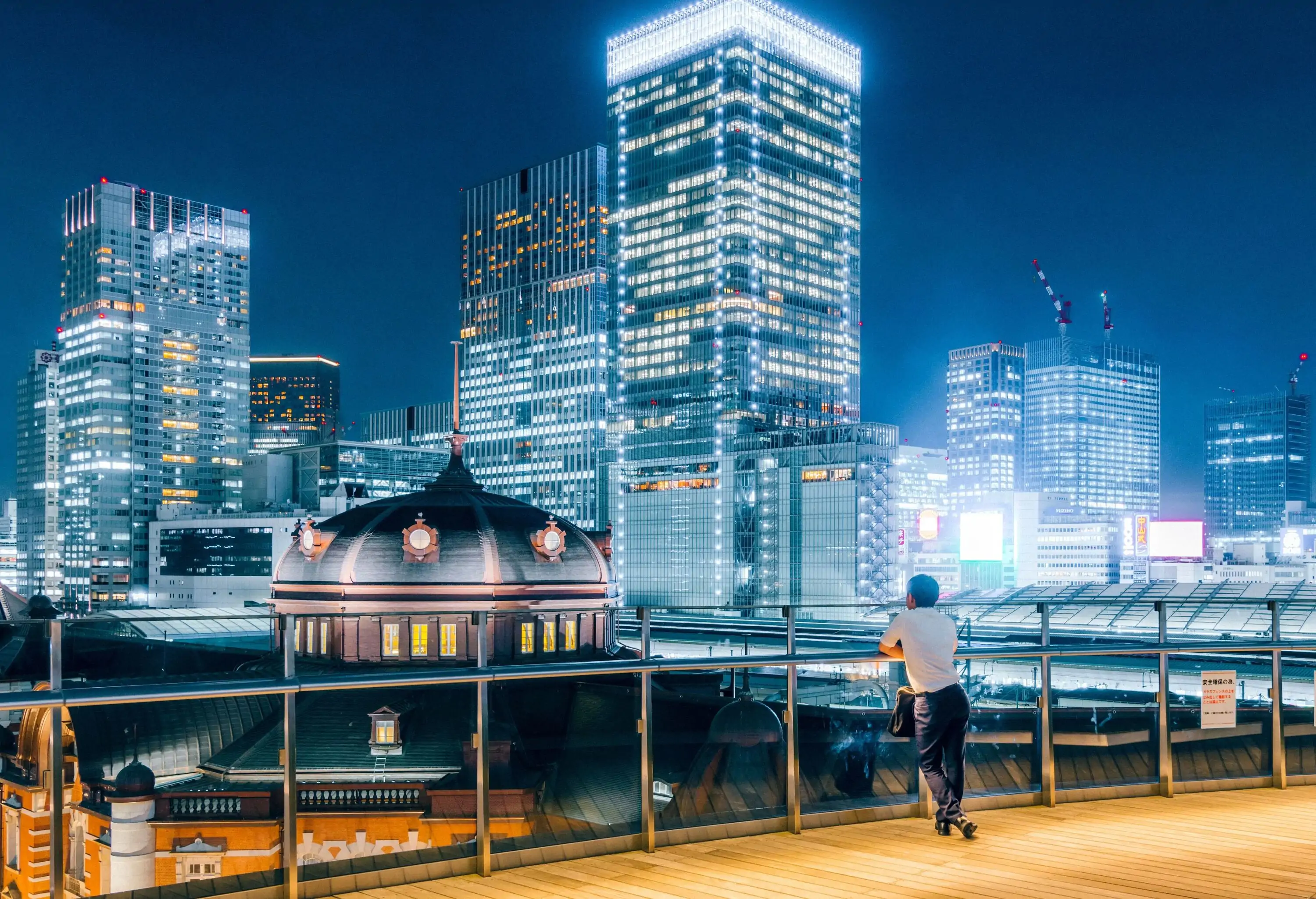 Man looking over a bridge at illuminated modern cityscape at night