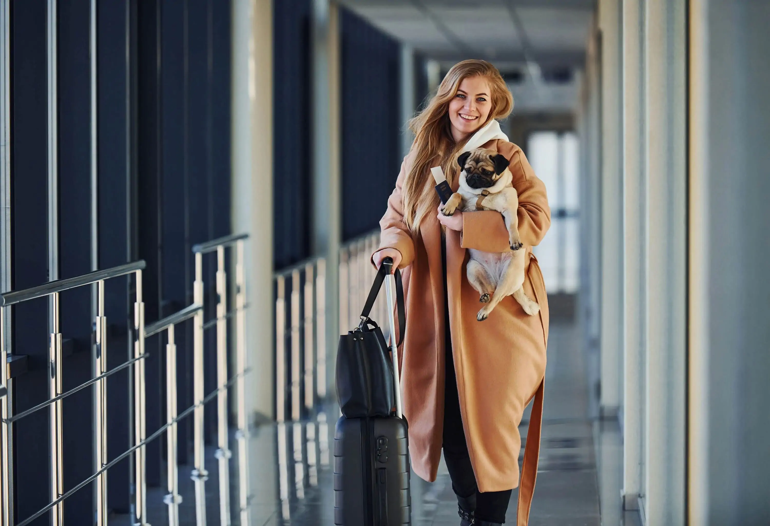 Young female passenger in warm clothes walking with her dog in airport hall.